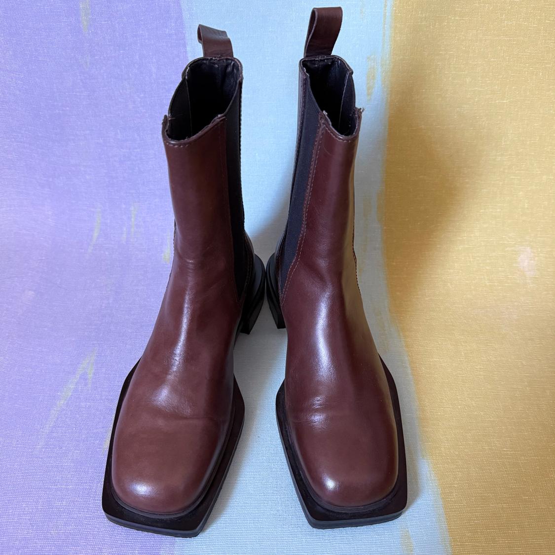 Square-toed brown leather boots on a pastel-colored background, including lilac and yellow.