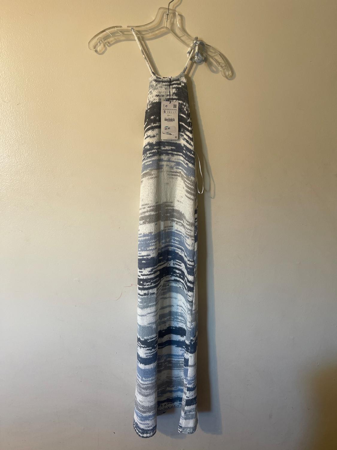 Long knit dress with abstract blue and white print, hanging on a clear hanger against a beige wall.