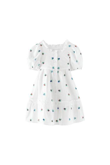 White dress with small embroidered flowers, short puffed sleeves, square neckline with frill, and front button fastening.