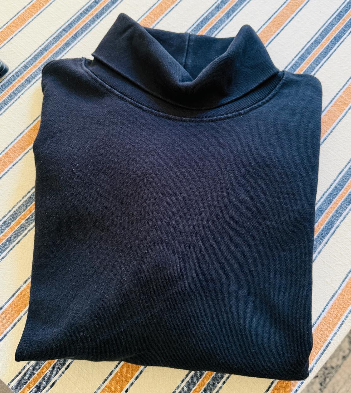 Black turtleneck sweater folded over a white, blue, and orange diagonal striped tablecloth. Relaxed atmosphere.