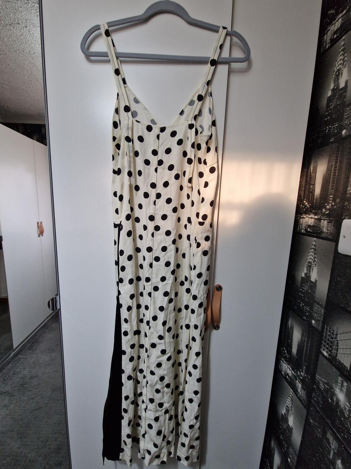 Long white dress with black polka dots and straps, with a side slit, hanging in a white wardrobe in natural light.