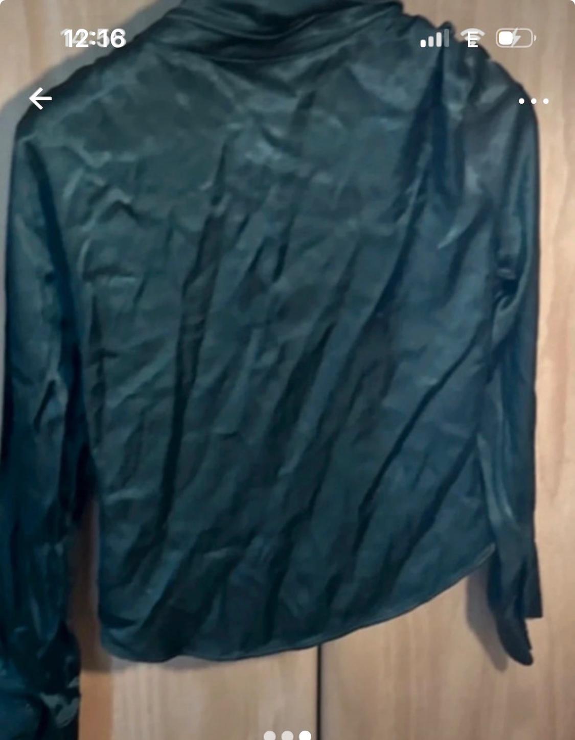 Dark-coloured crinkled shirt hanging over a wooden door. Phone screen visible with time 12:36.
