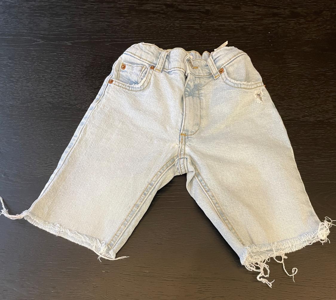 Light blue denim shorts with an elasticated waist and frayed hems, on a dark wooden surface.
