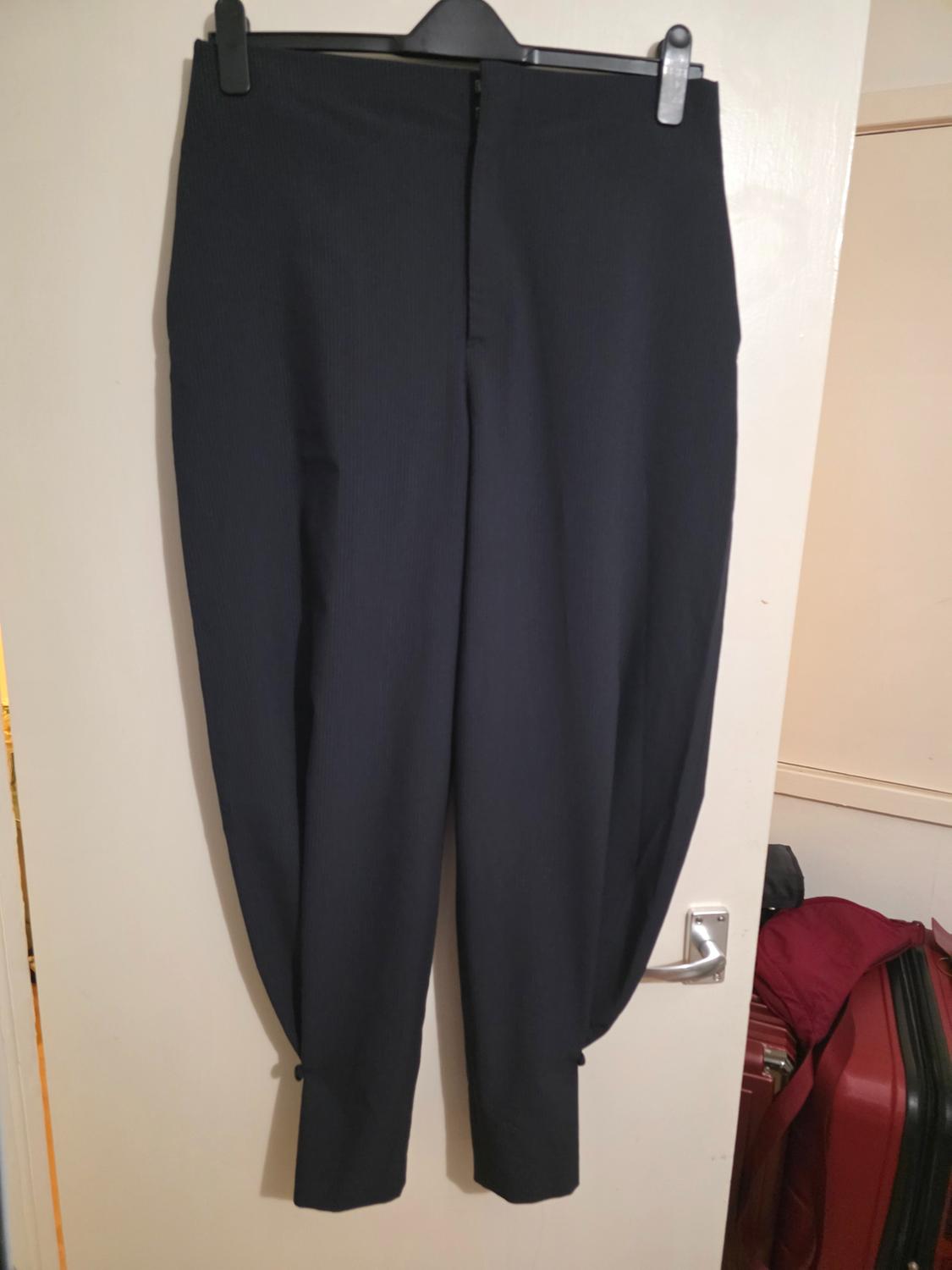 Black trousers hanging on a hanger over a white door. In the background, red suitcases are partially visible.