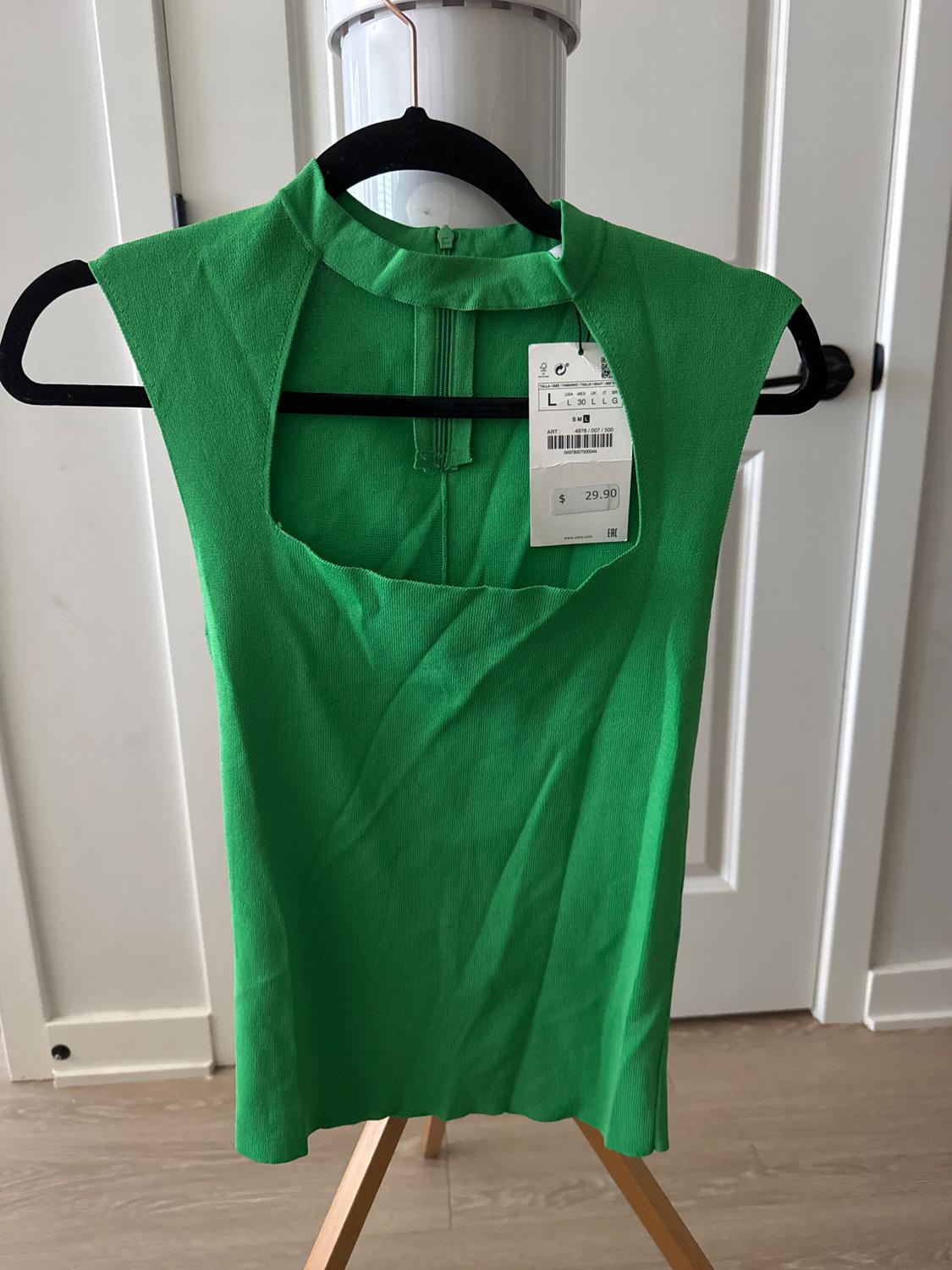Green sleeveless top with a high neck and front slit, hanging on a black hanger. Visible tag with a price of $29.90.