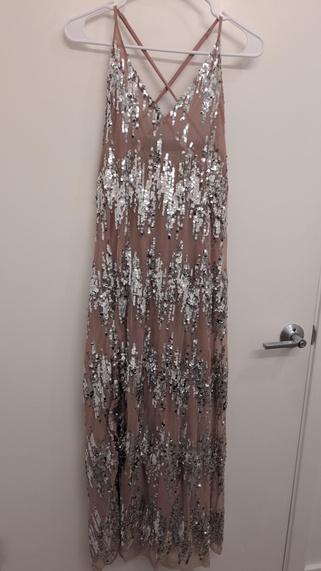 Spaghetti strap dress with silver sequins on a pink background, hanging on a white hanger in front of a white door.