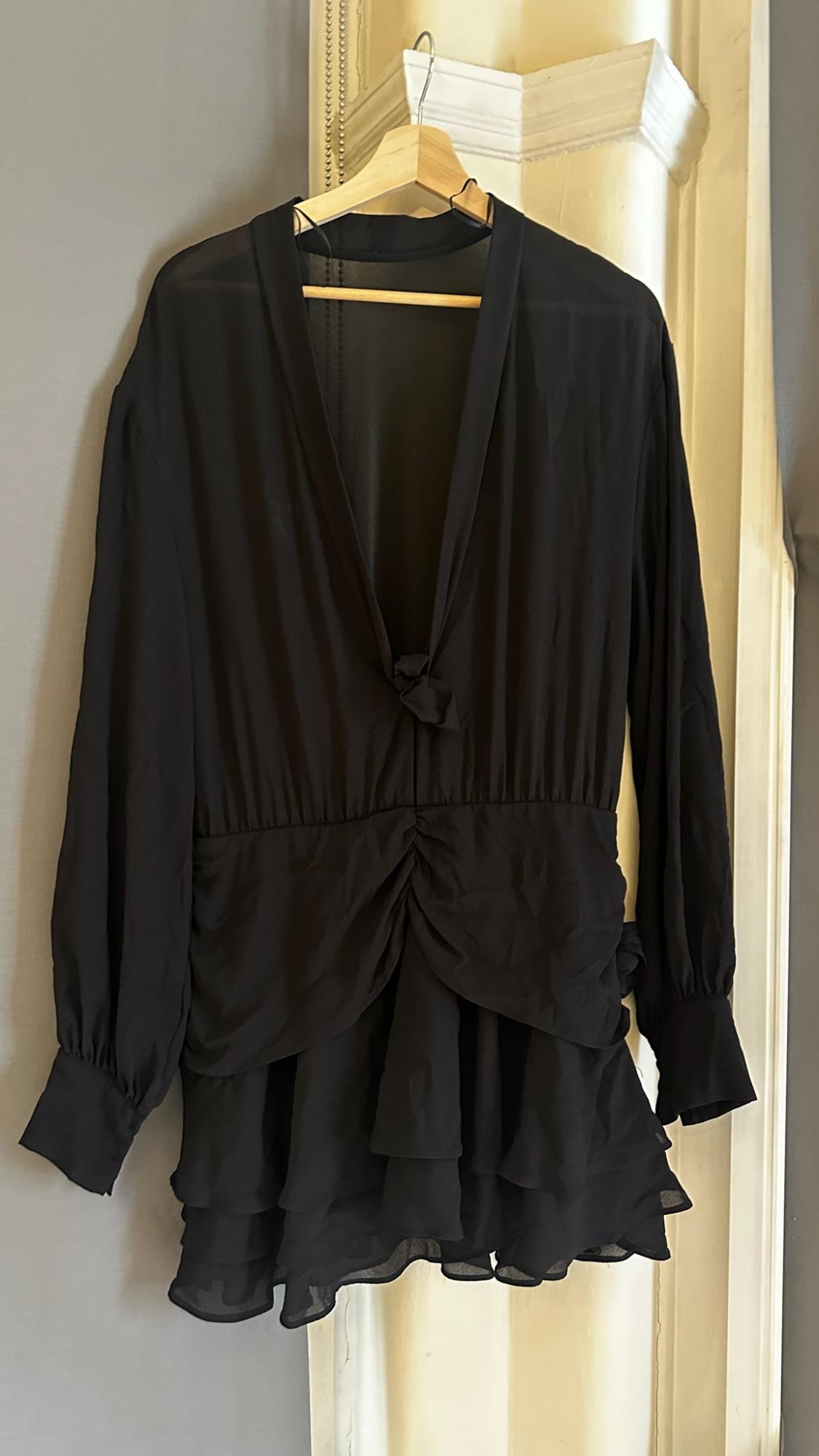 Black dress hanging on a hanger. V-neckline with a tie, long sleeves, gathered waist and a tiered ruffle skirt.