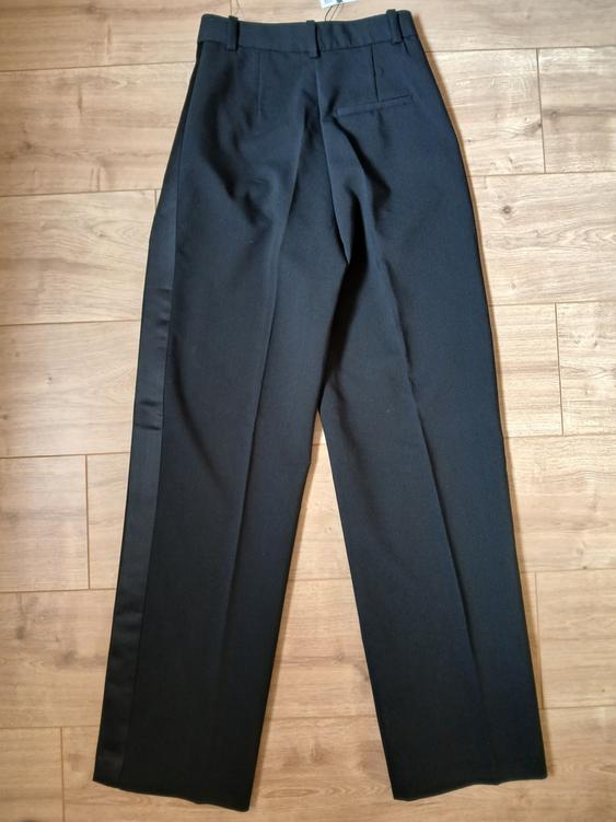 Black dress trousers with a waistband and back pockets, placed on a light wooden floor.