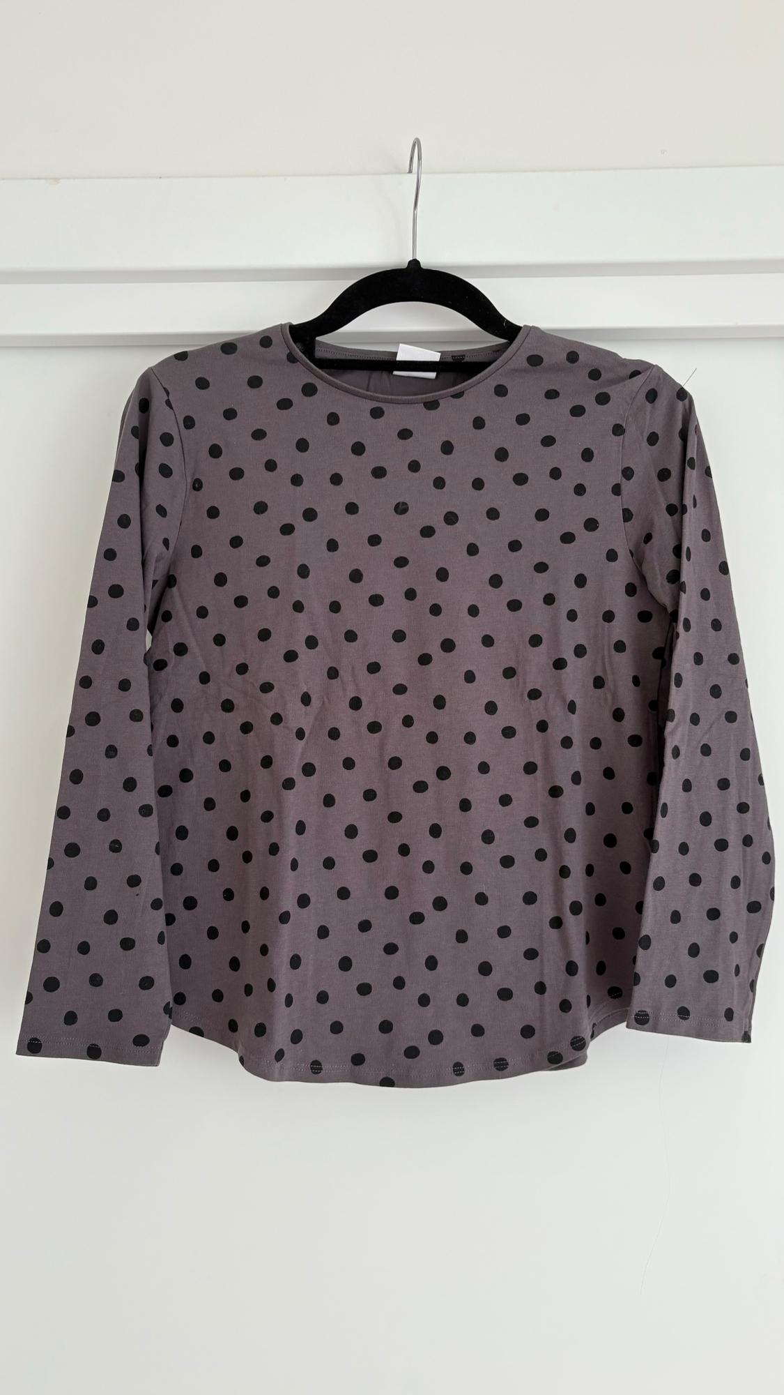 Grey long-sleeved T-shirt with black polka dots hanging on a black hanger against a white background.