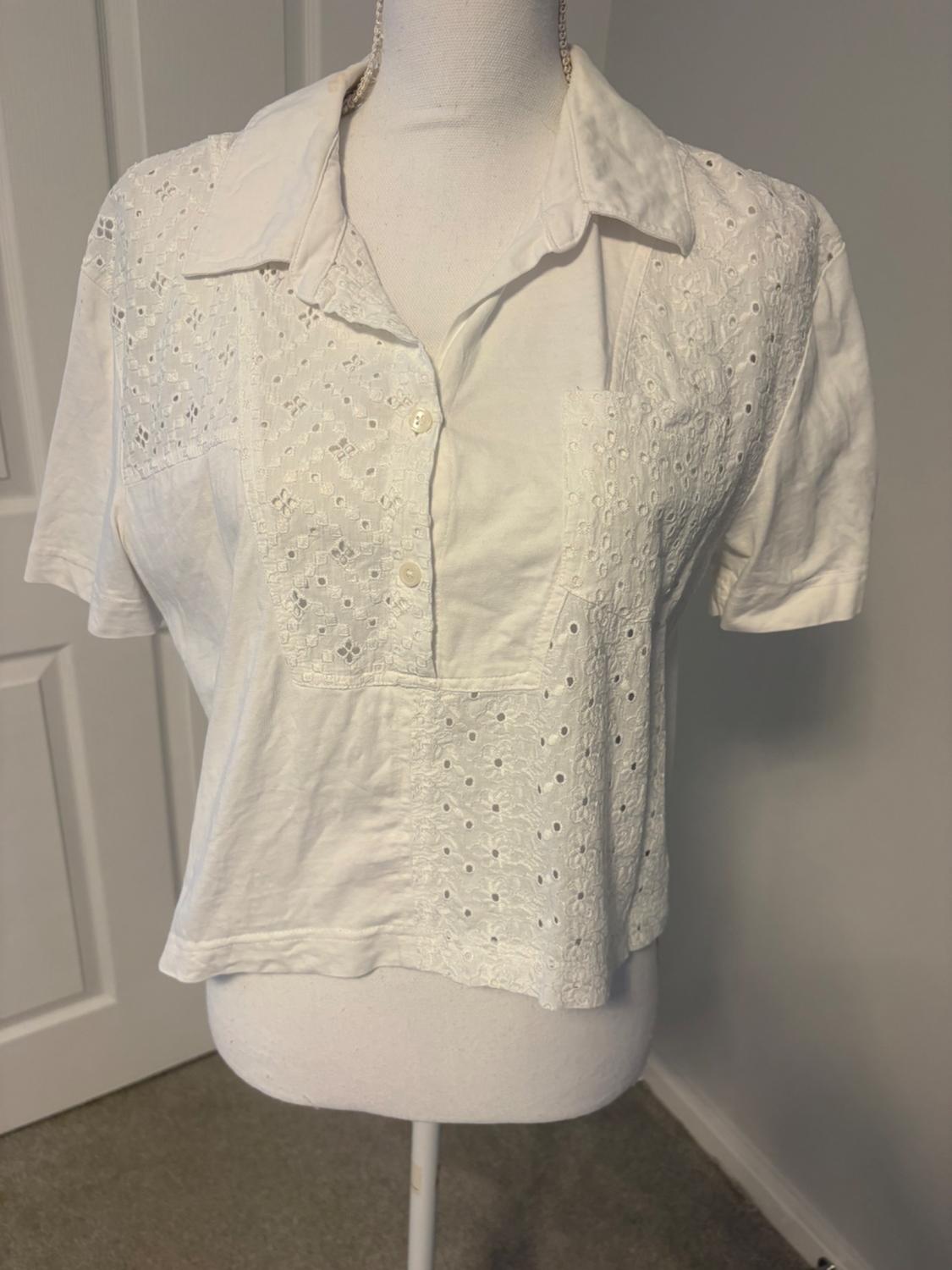 Short-sleeved white shirt with a collar and broderie anglaise detailing on a mannequin in a room with a white door in the background.