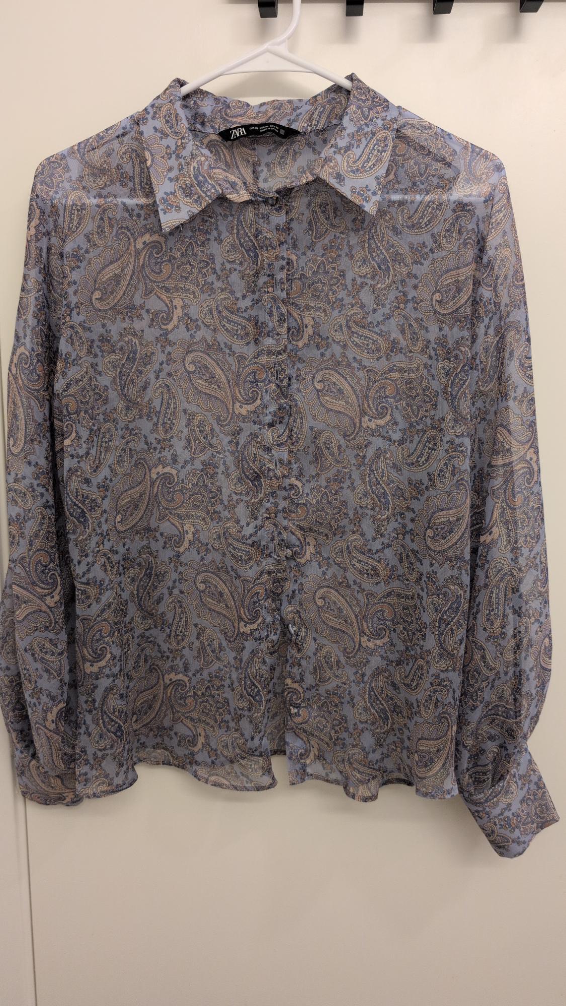 Long-sleeved shirt with a paisley print in shades of blue and beige, hanging on a white hanger.