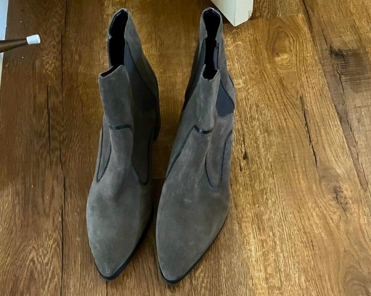 Grey suede boots with pointed toes on a wooden floor. Elegant and modern design, viewed from above.
