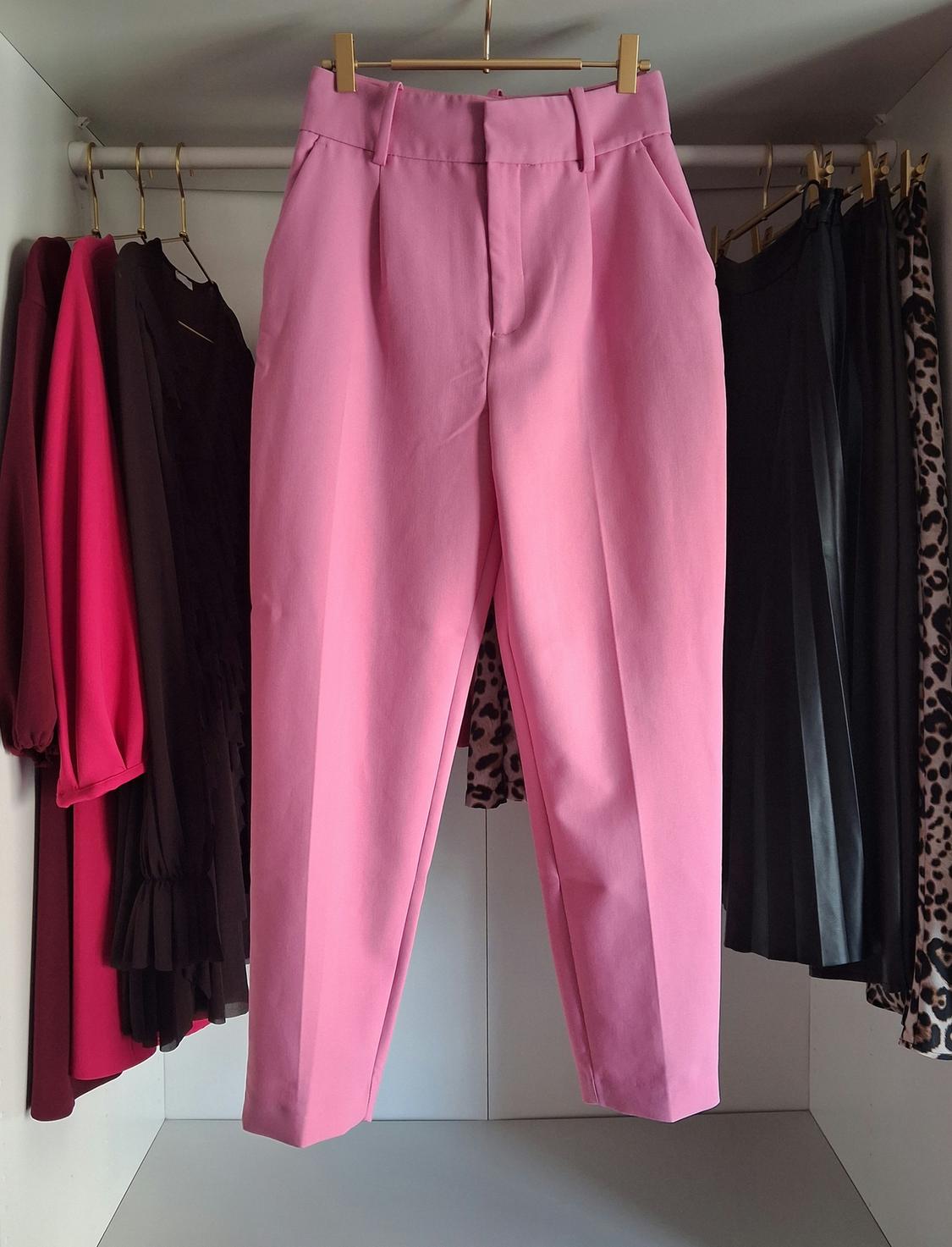 Pink trousers hanging in a wardrobe, surrounded by various garments, including dresses in dark tones and leopard print.