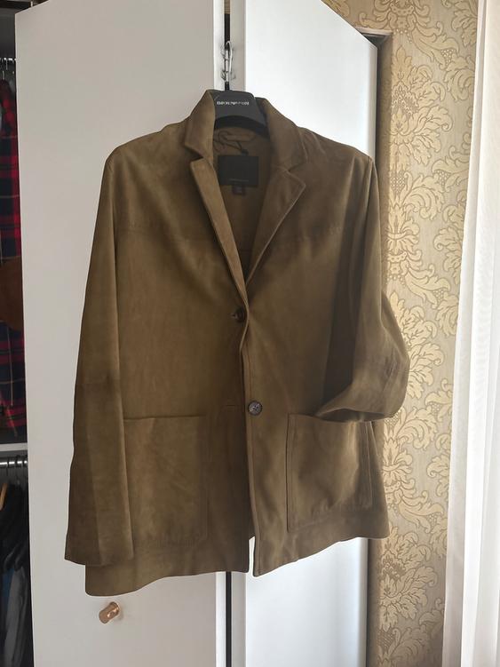 Brown jacket hanging on a hanger inside a white closet. Background with decorative beige wallpaper.