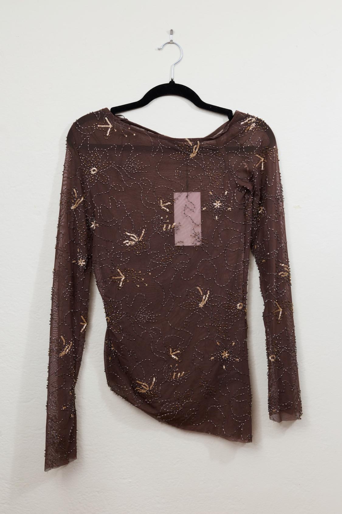 Long-sleeve brown manga top in sheer fabric, hanging on a black hanger against a white background. Decorated with beads and sequins.