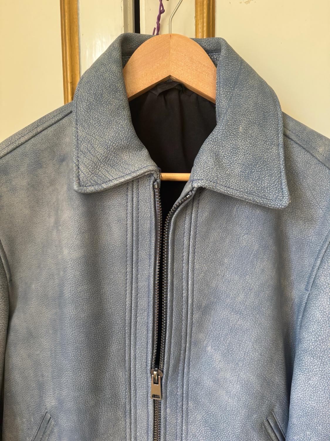 Close-up of a light blue jacket with a distressed texture, collar and front zip, hanging on a wooden hanger.