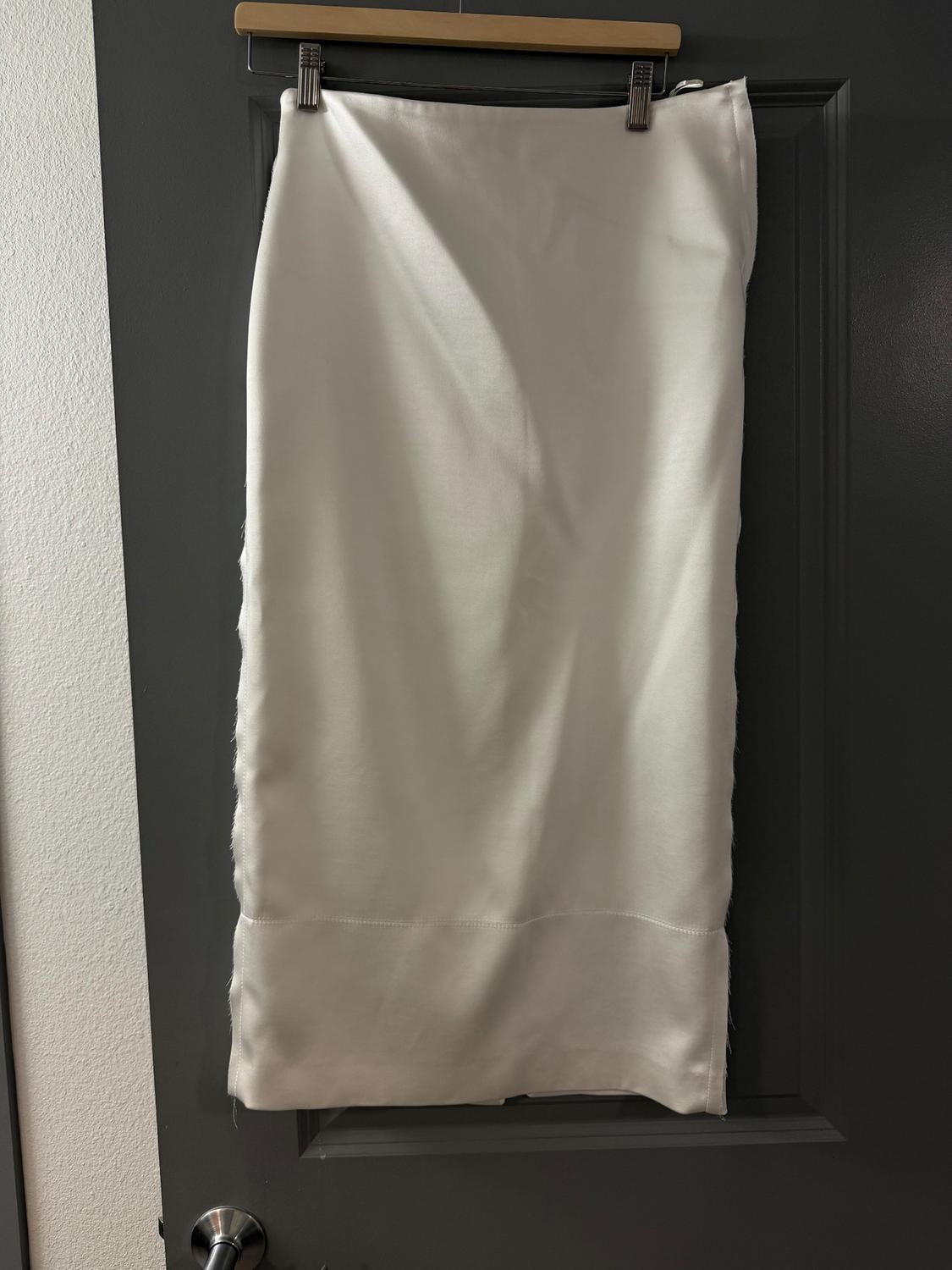 White skirt hanging on a hanger over a grey door. The fabric is plain and has a visible hem at the bottom.