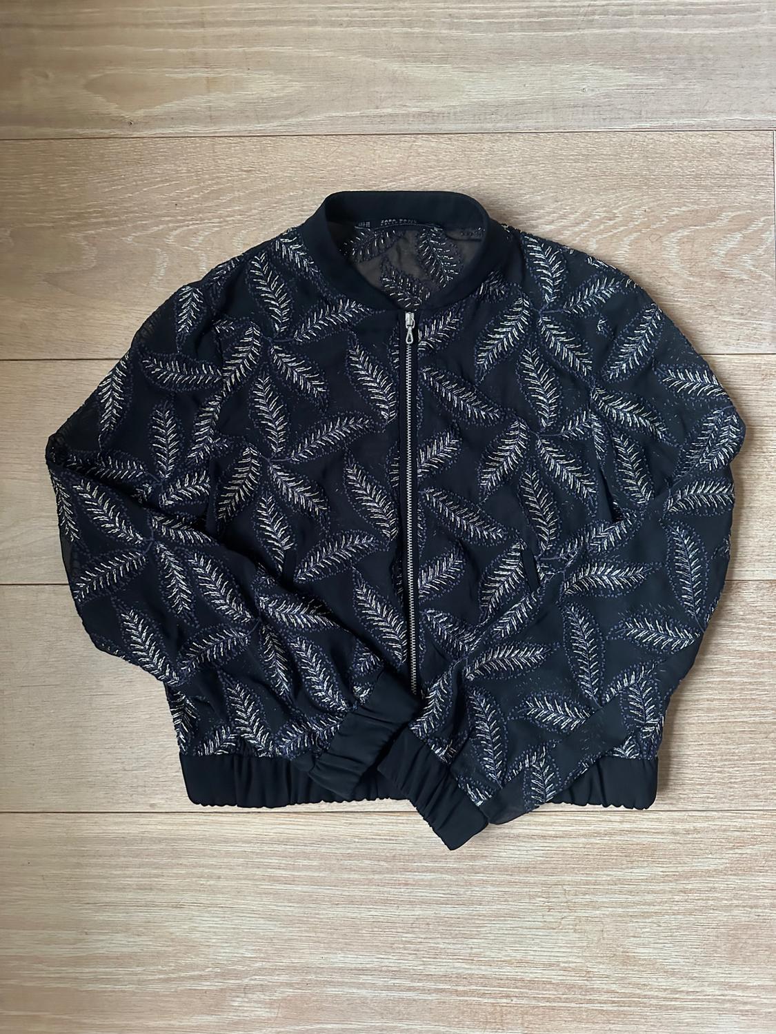 Front view of a black jacket with embossed leaf print and zip fastening.