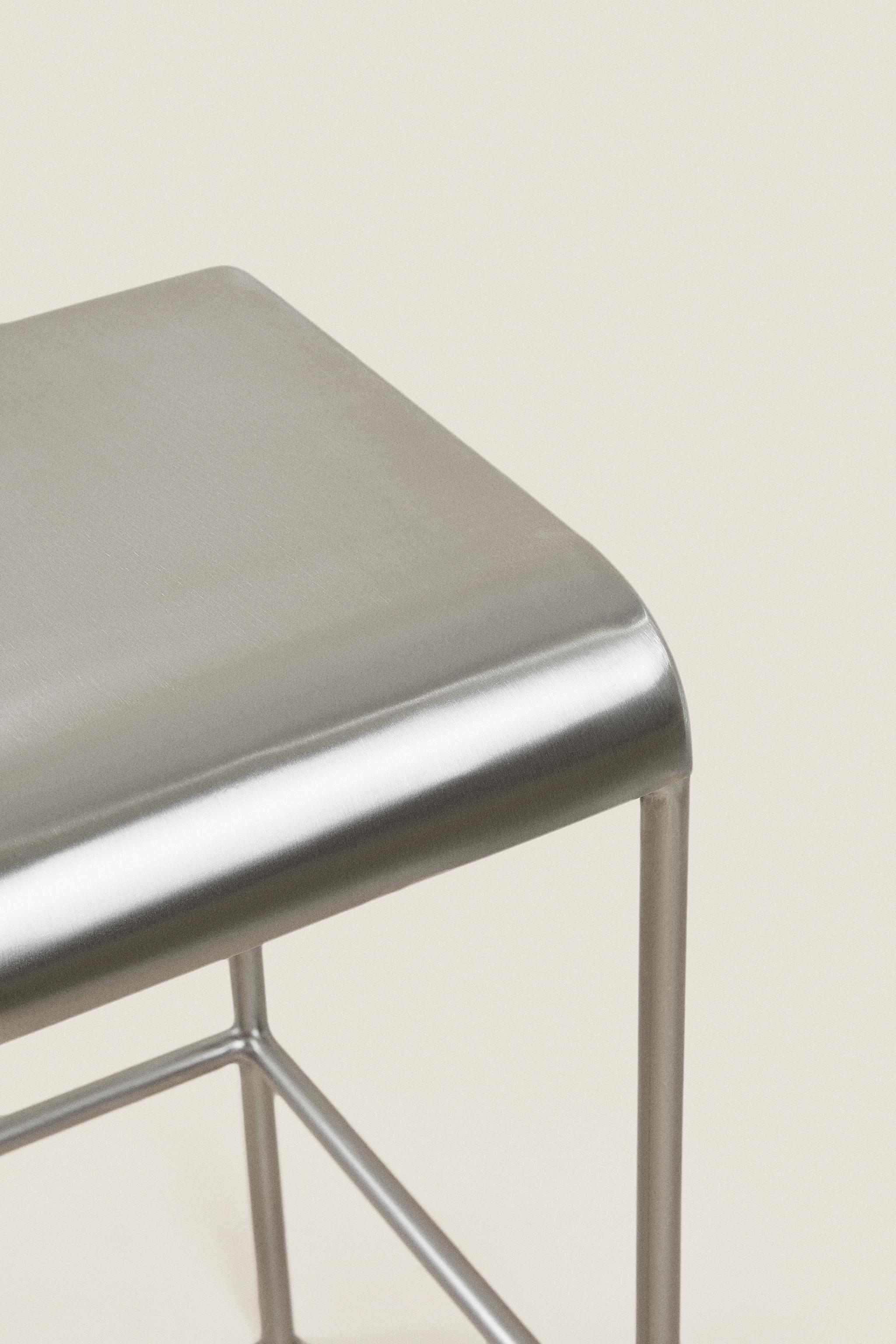 Close-up detail of the seat and leg structure of a matte silver bar stool.
