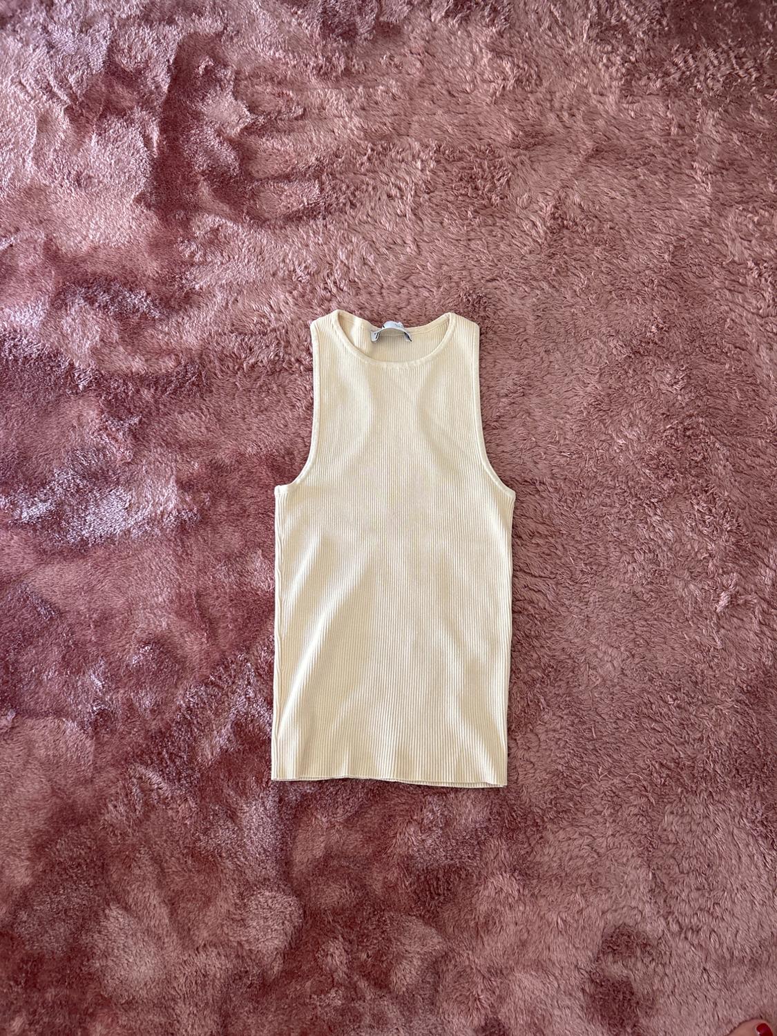 Cream ribbed sleeveless top, laid out on a pink fluffy textured rug. Flat lay composition in a casual and relaxed style.