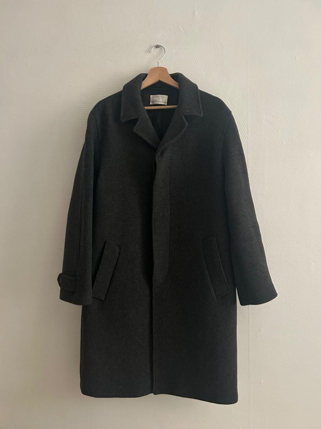 Black wool coat hanging on a wooden hanger against a white wall. Classic design with lapels and side pockets.