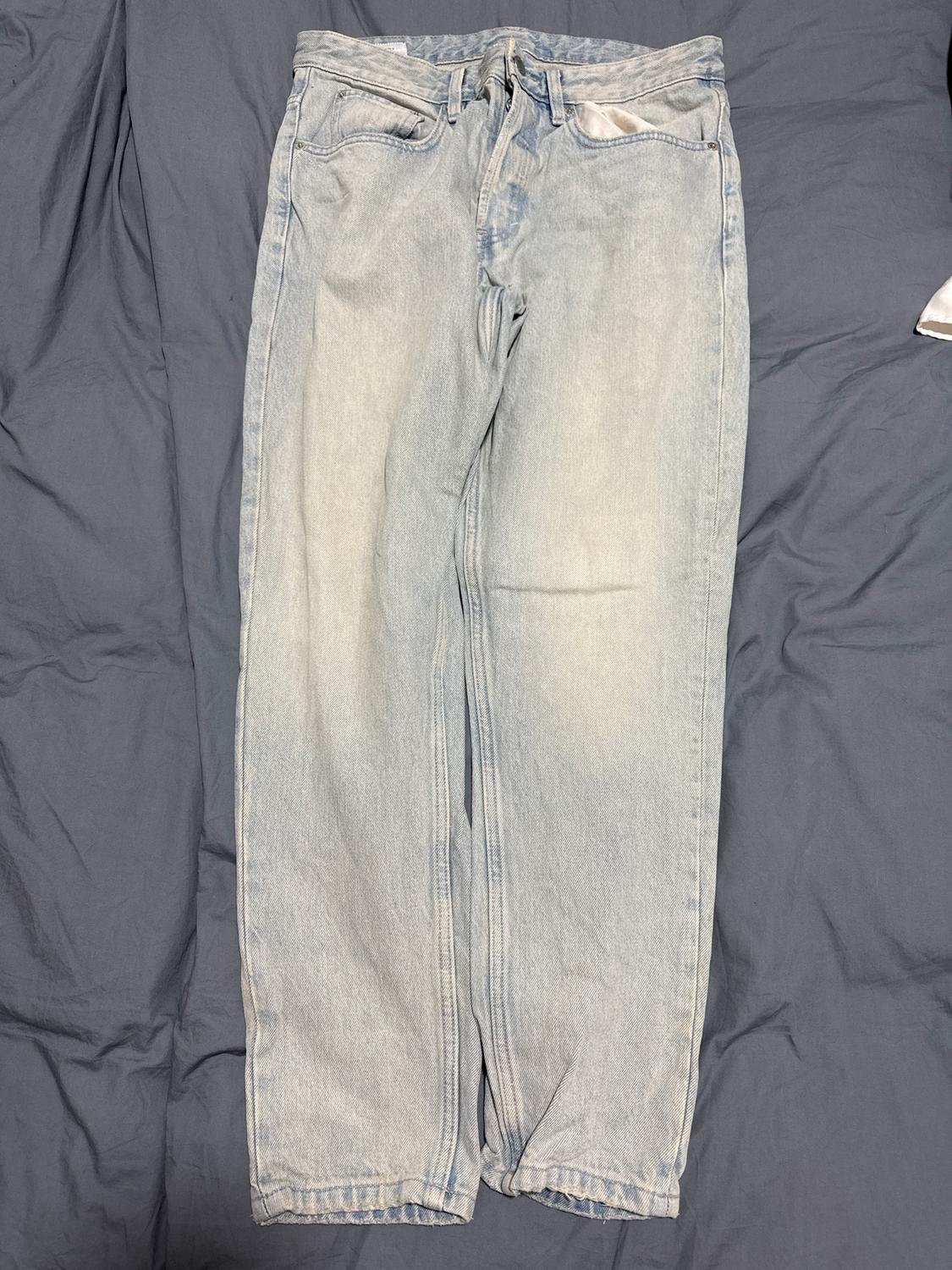 Light denim jeans placed on a grey surface. Classic design with front and back pockets.