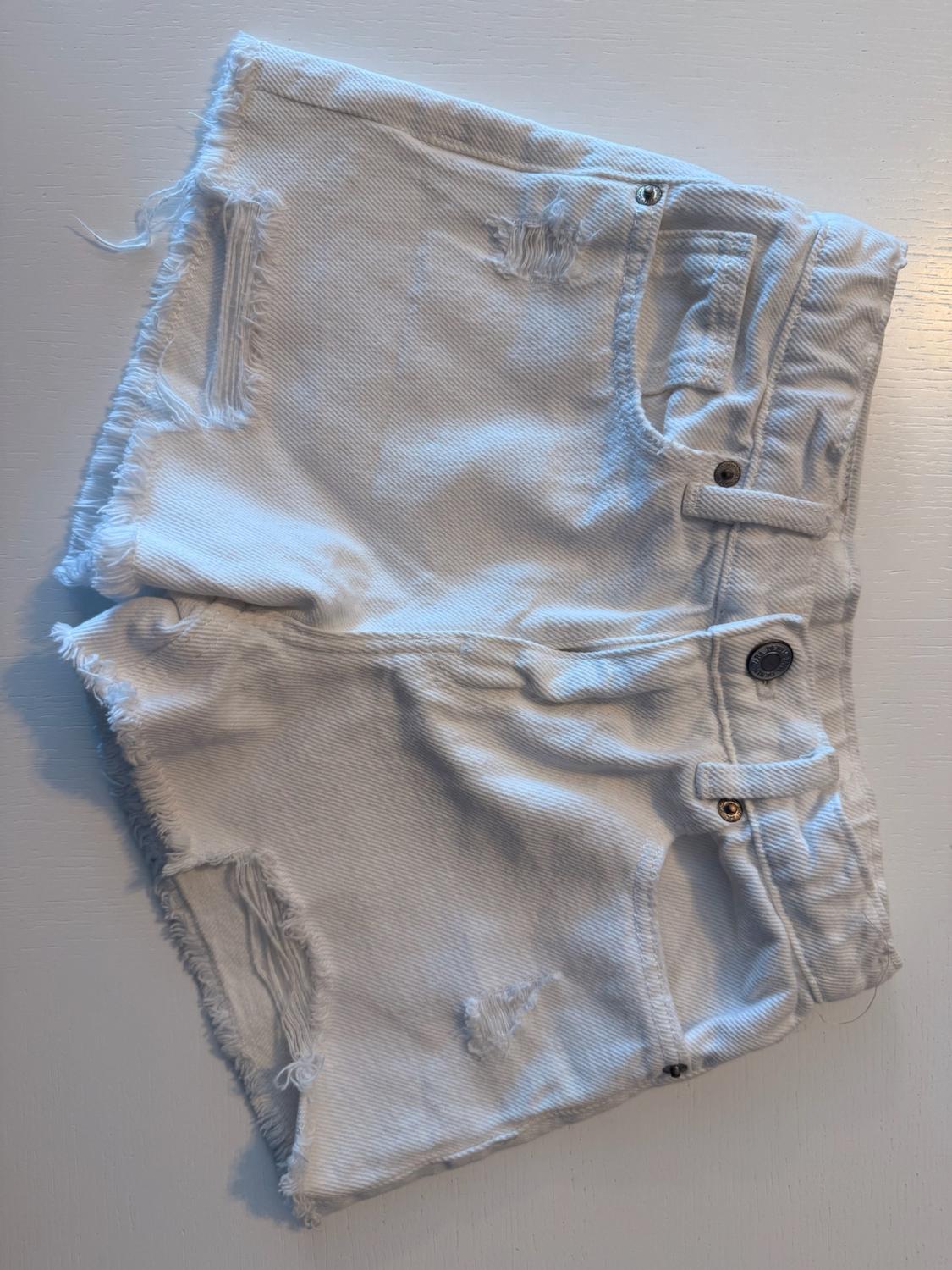 White denim shorts with distressed details and a raw hem, on a white surface. Casual and relaxed style.