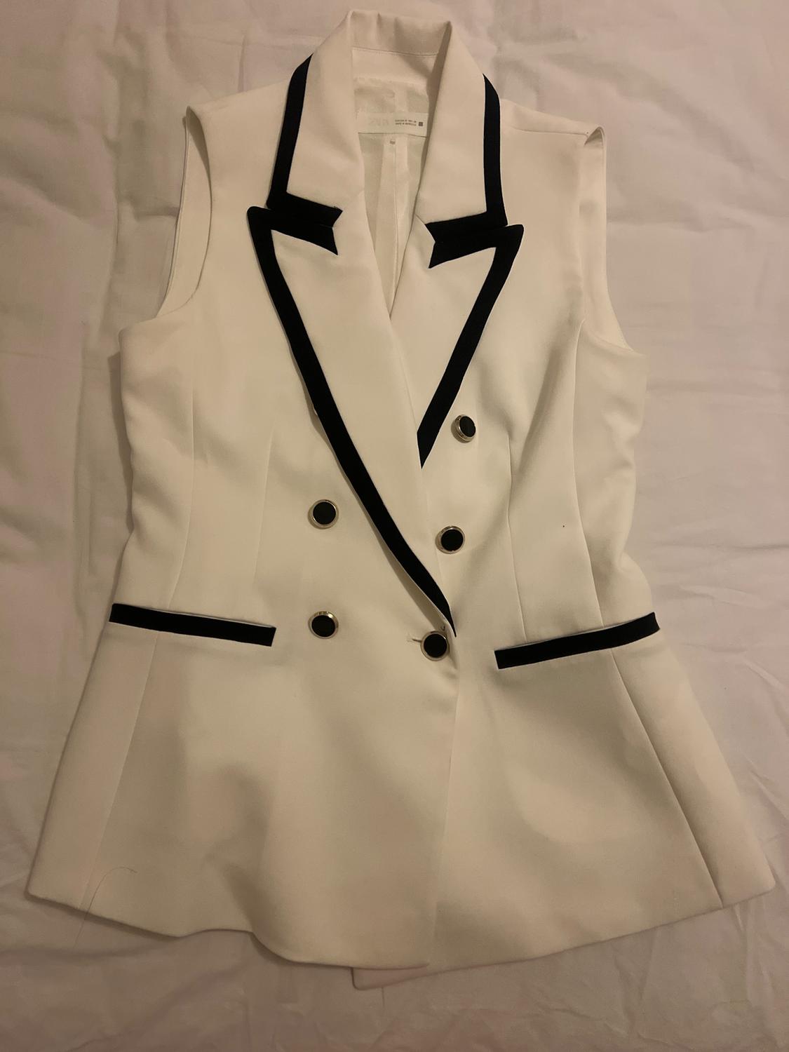 White sleeveless waistcoat with black lapels and gold buttons, on a white background.