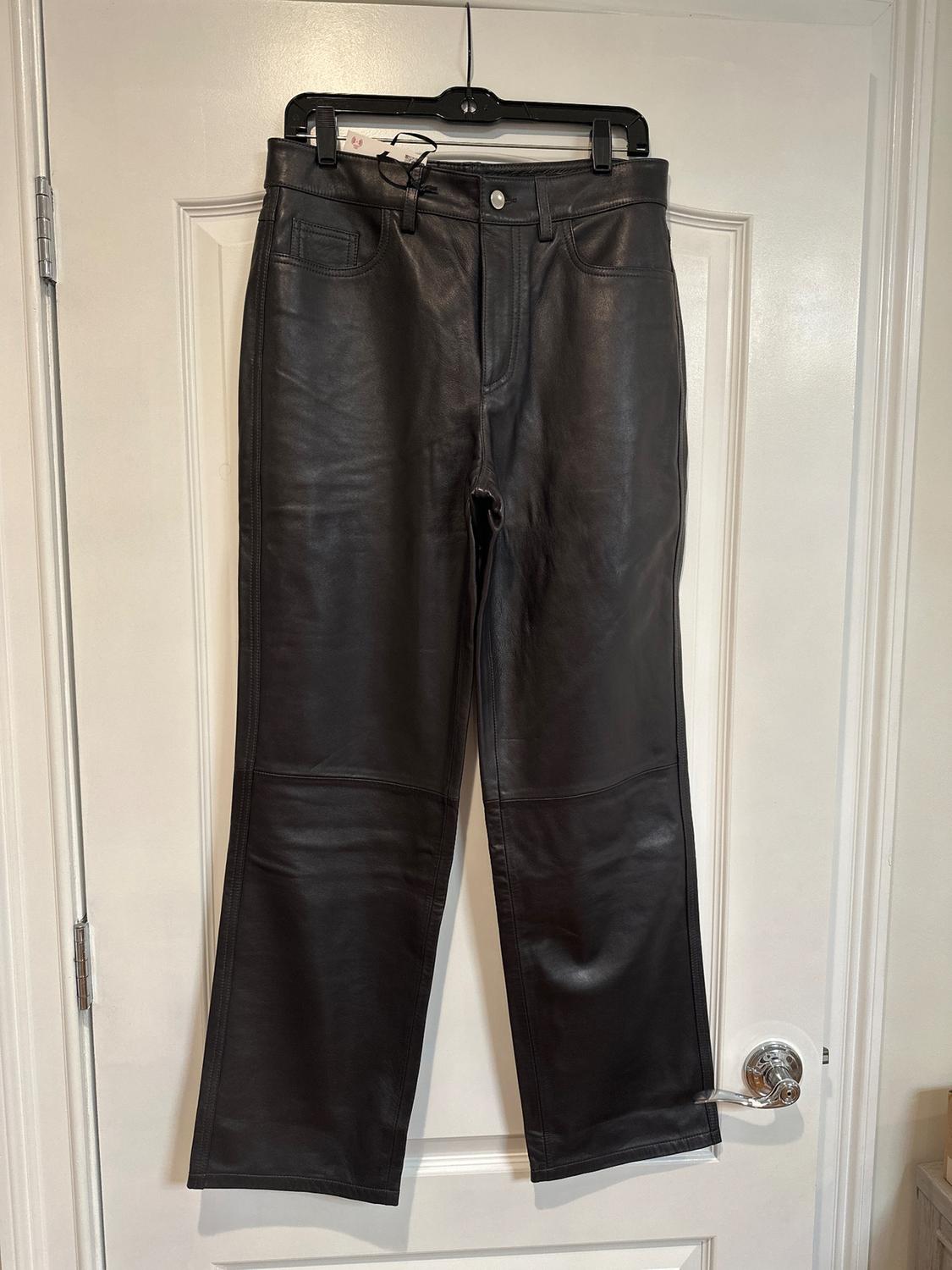 Black leather pants hanging on a black hanger over a white door. Classic design with pockets and button closure.