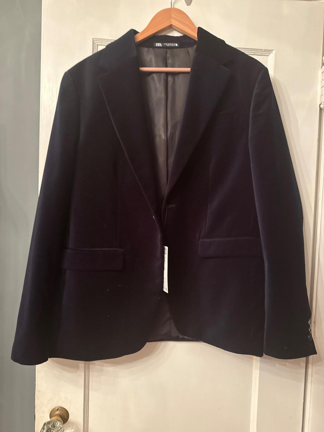 Black jacket hanging on a wooden hanger over a white door. Label visible inside the collar.