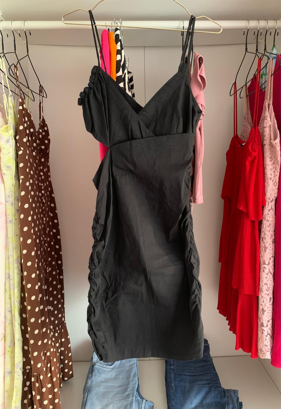 Black dress with thin straps hanging in a wardrobe next to other dresses of various colours and patterns.