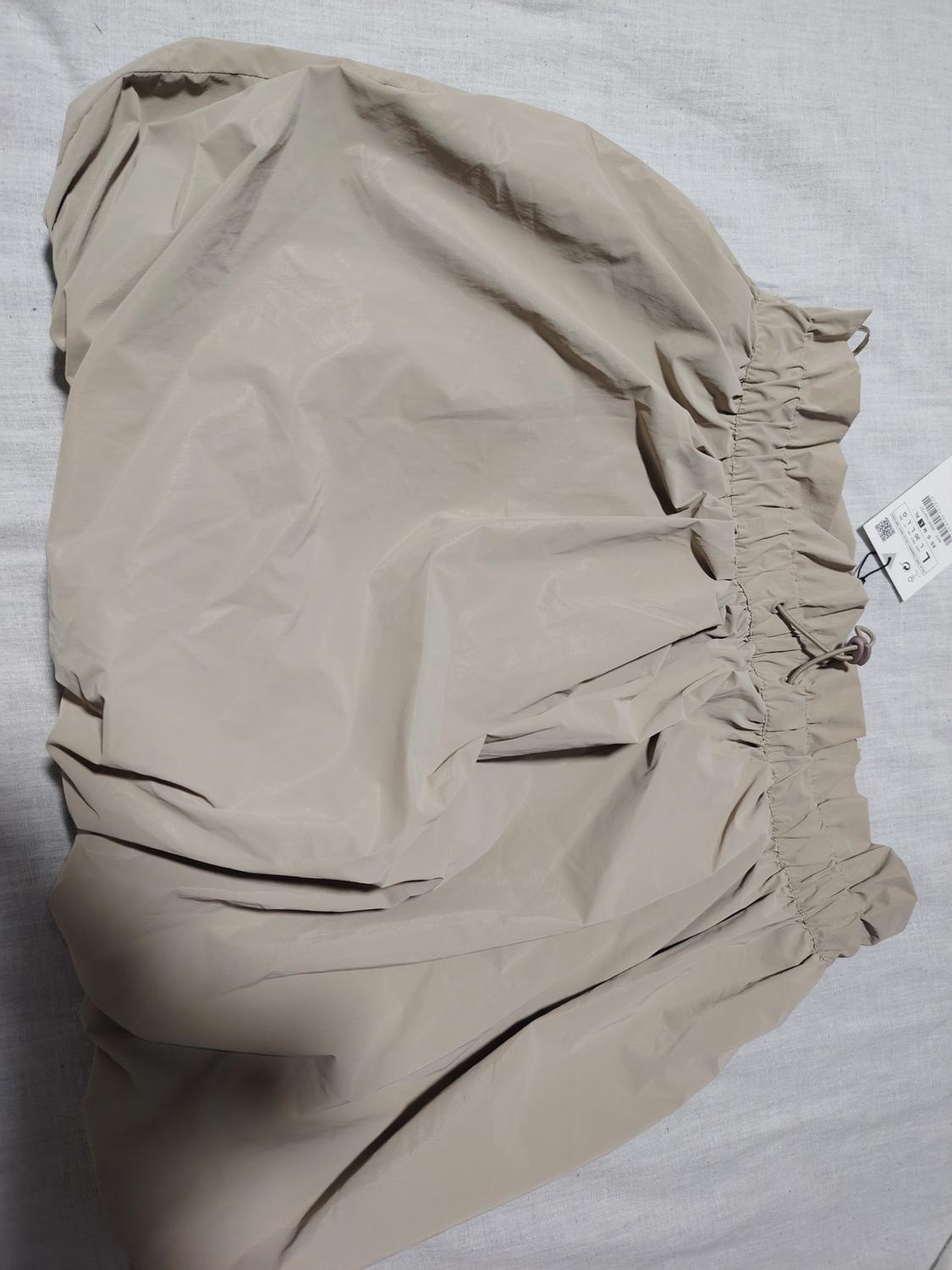 Beige crinkled skirt with elasticated waistband on a grey surface. Visible label with barcode and small text.