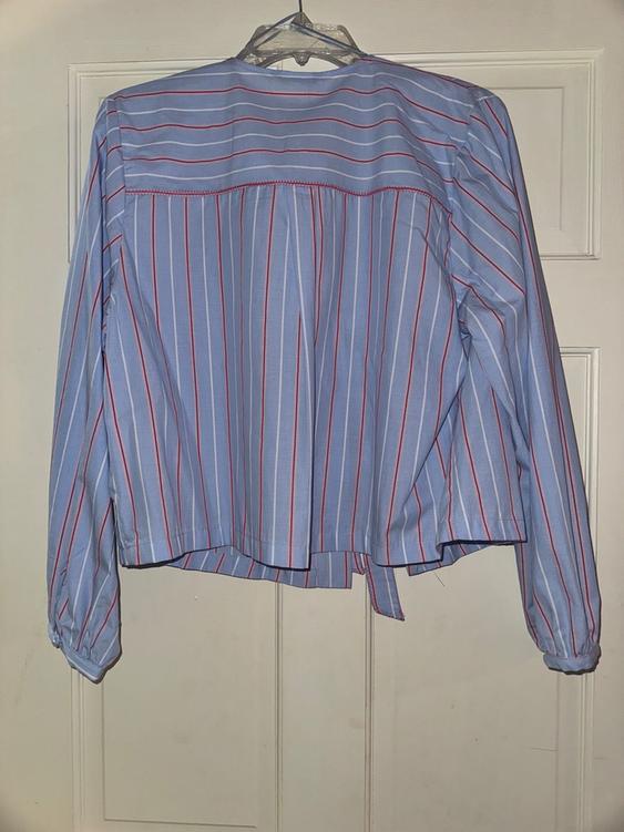 Blue and red striped shirt hanging on a clear hanger over a white door. Long sleeves and loose design.