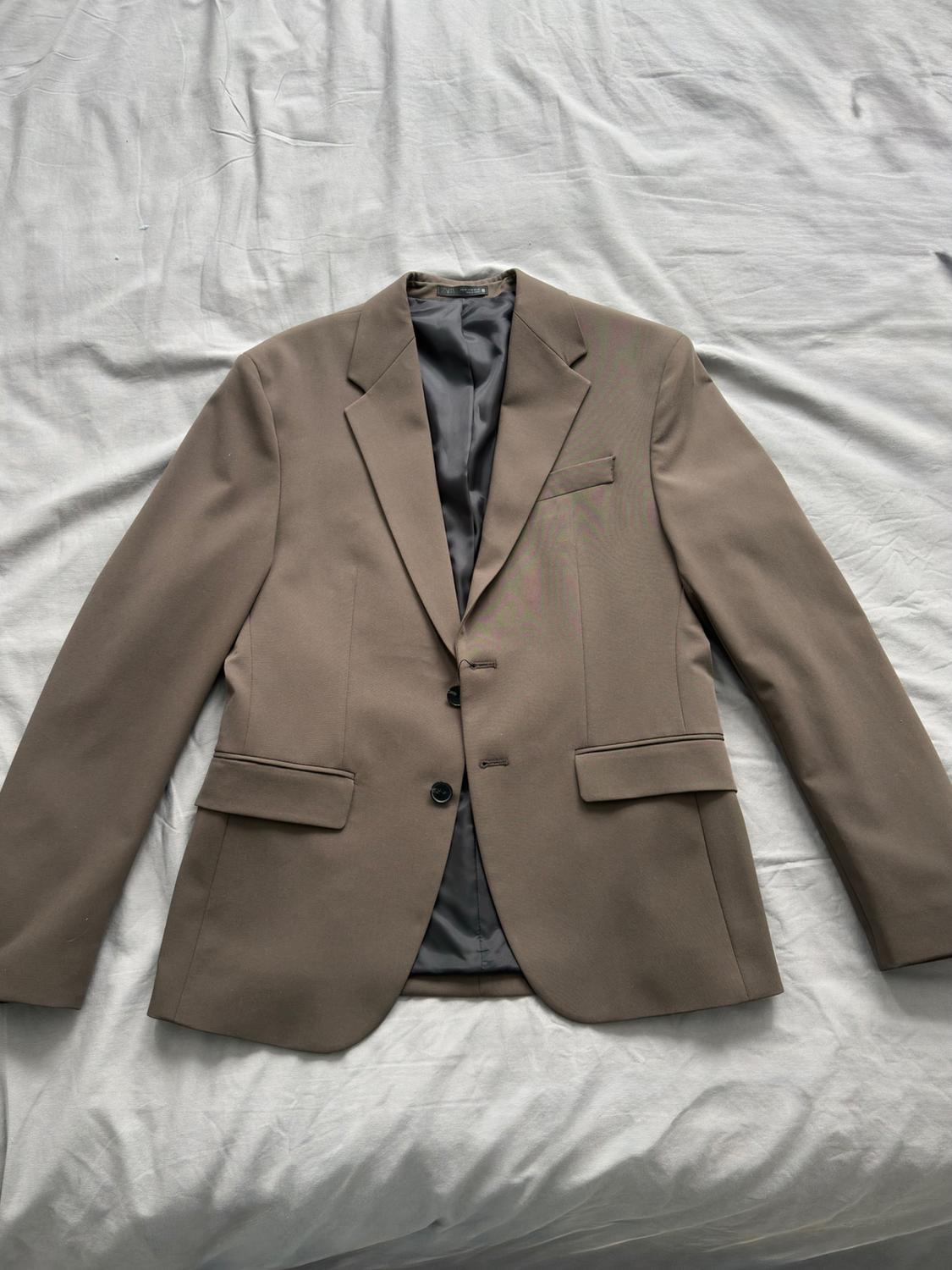 Light brown jacket with two buttons and classic lapels, placed on a crumpled white surface.