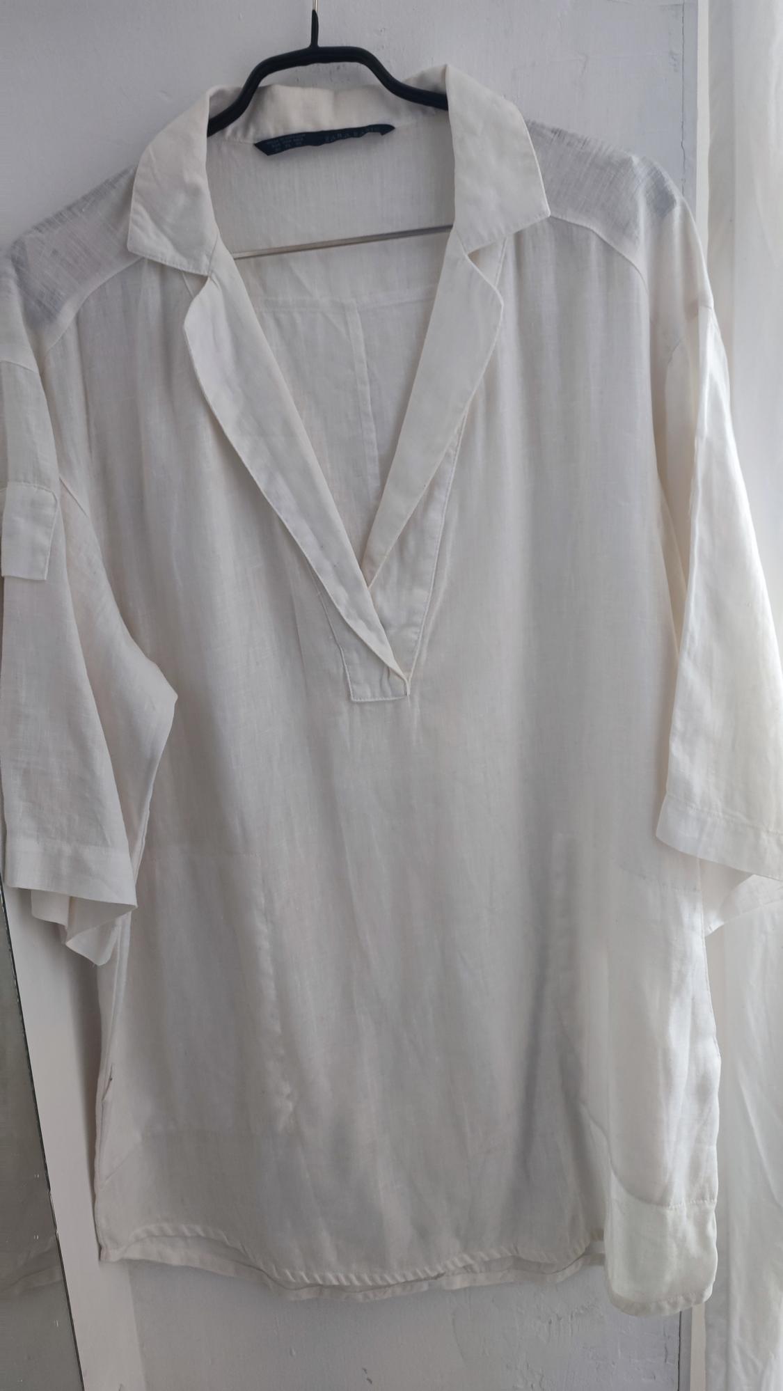 White, long-sleeved shirt hanging on a black hanger, with an open collar and light fabric, on a white background.