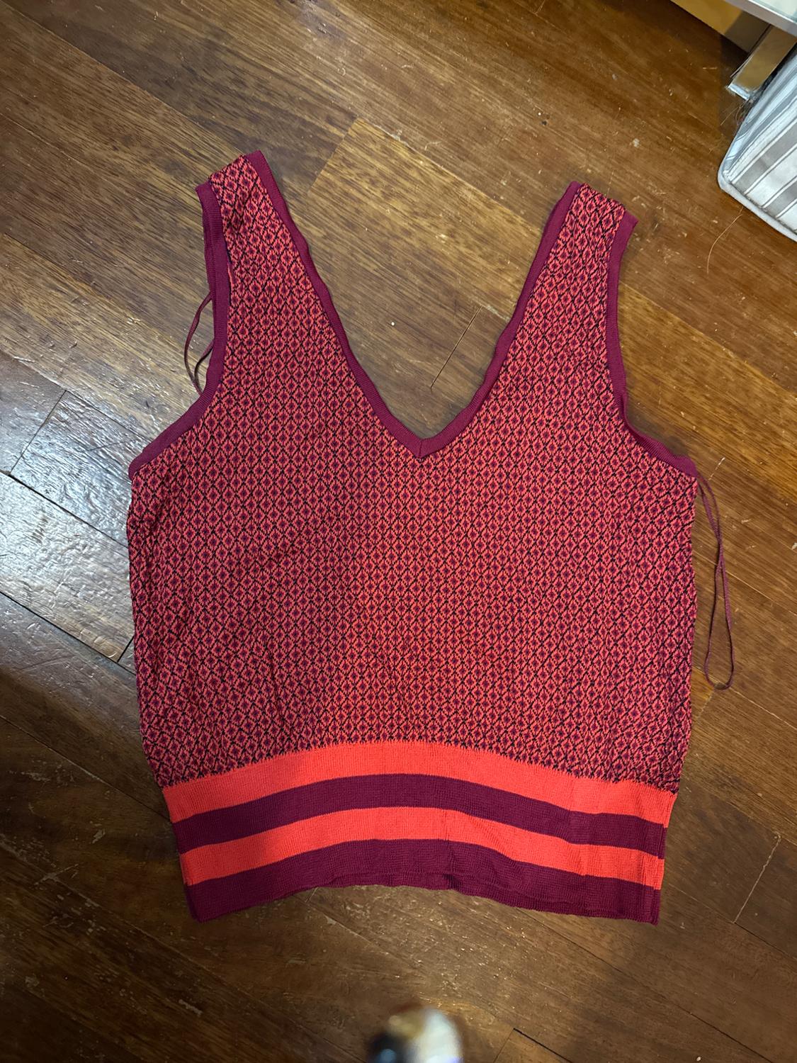 Red sleeveless top with a geometric pattern and V-neck, on a wooden floor. Bottom with red and purple horizontal stripes.
