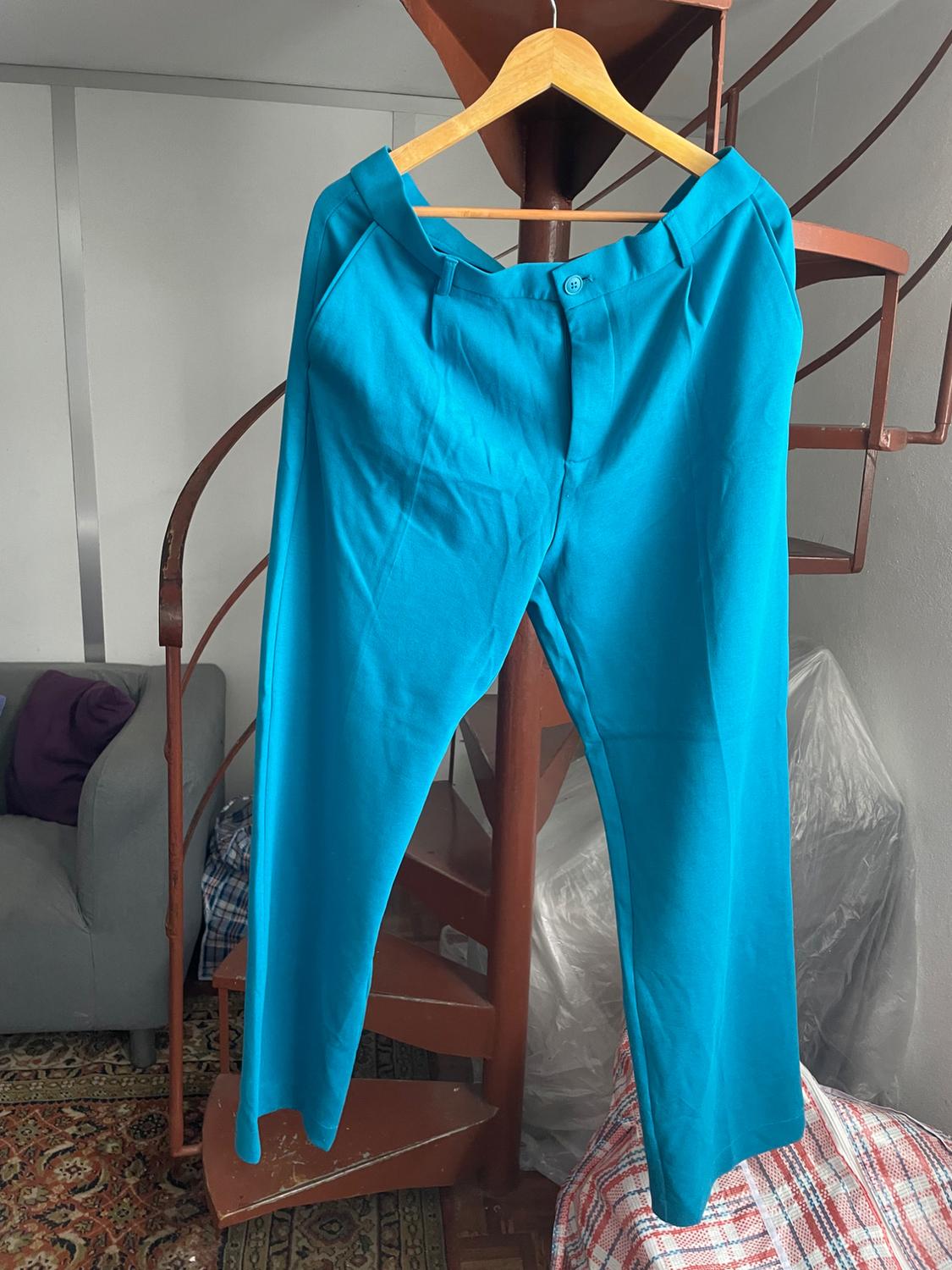 Blue trousers hanging on a wooden hanger over a brown spiral staircase, with a grey sofa in the background.