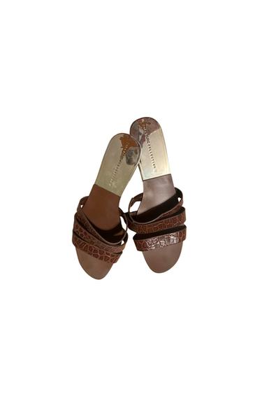 Brown sandals with textured straps and metallic sole. Visible text: "VANESSA COLLECTION". White background.