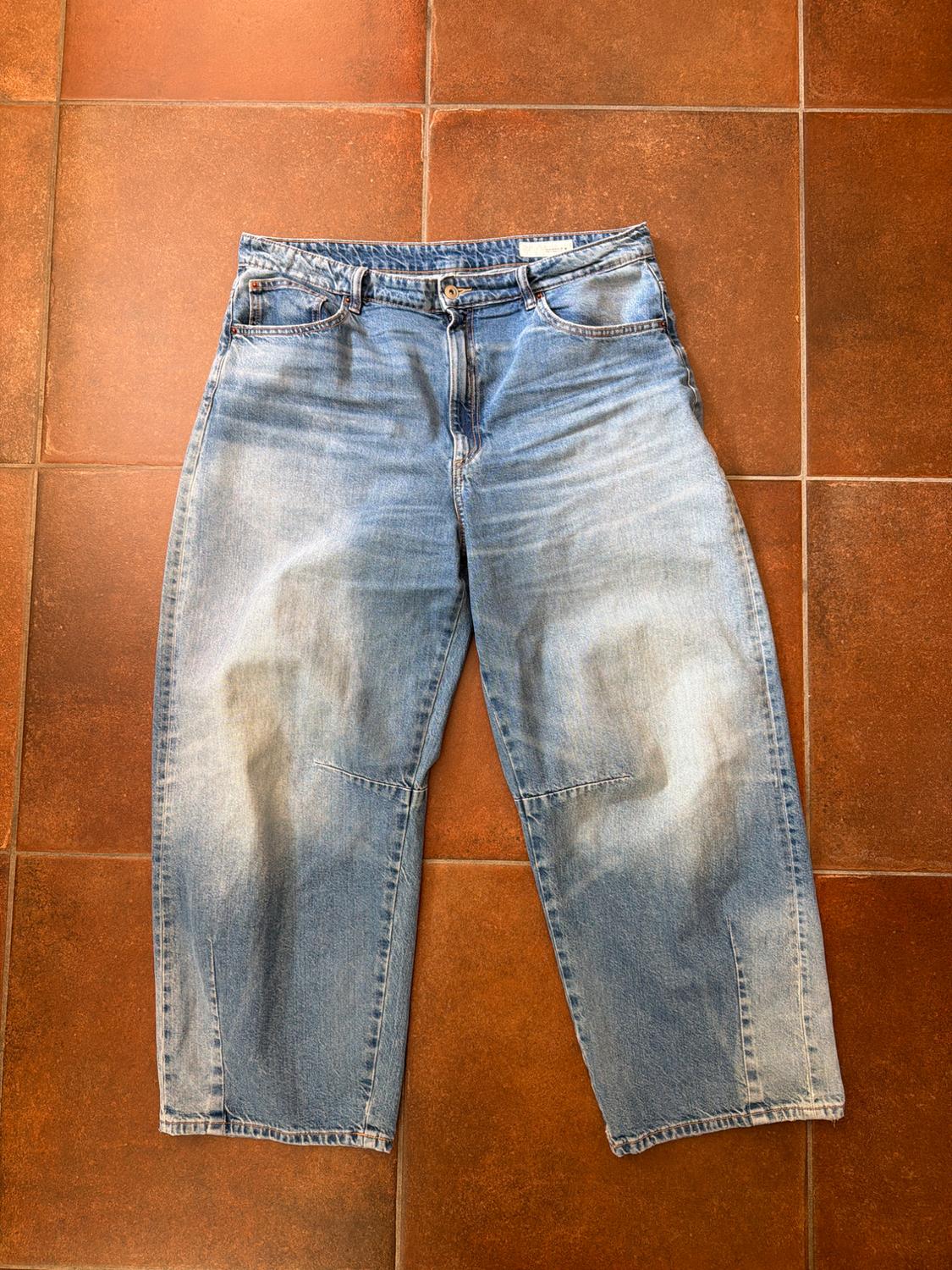 Worn blue jeans on a brown tiled floor. Straight cut and high waist, with front and back pockets.