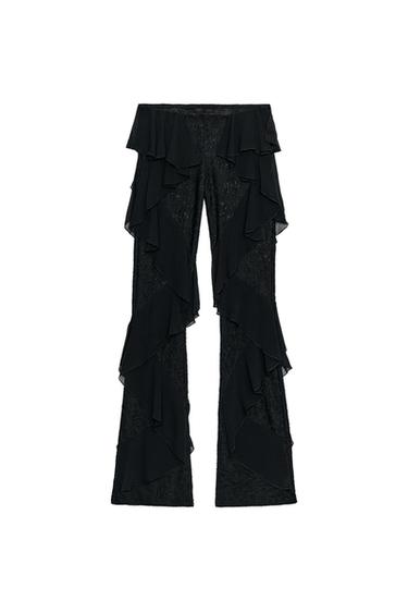 Front view of long black trousers. The decorative ruffles running down the front of both legs are a prominent feature.