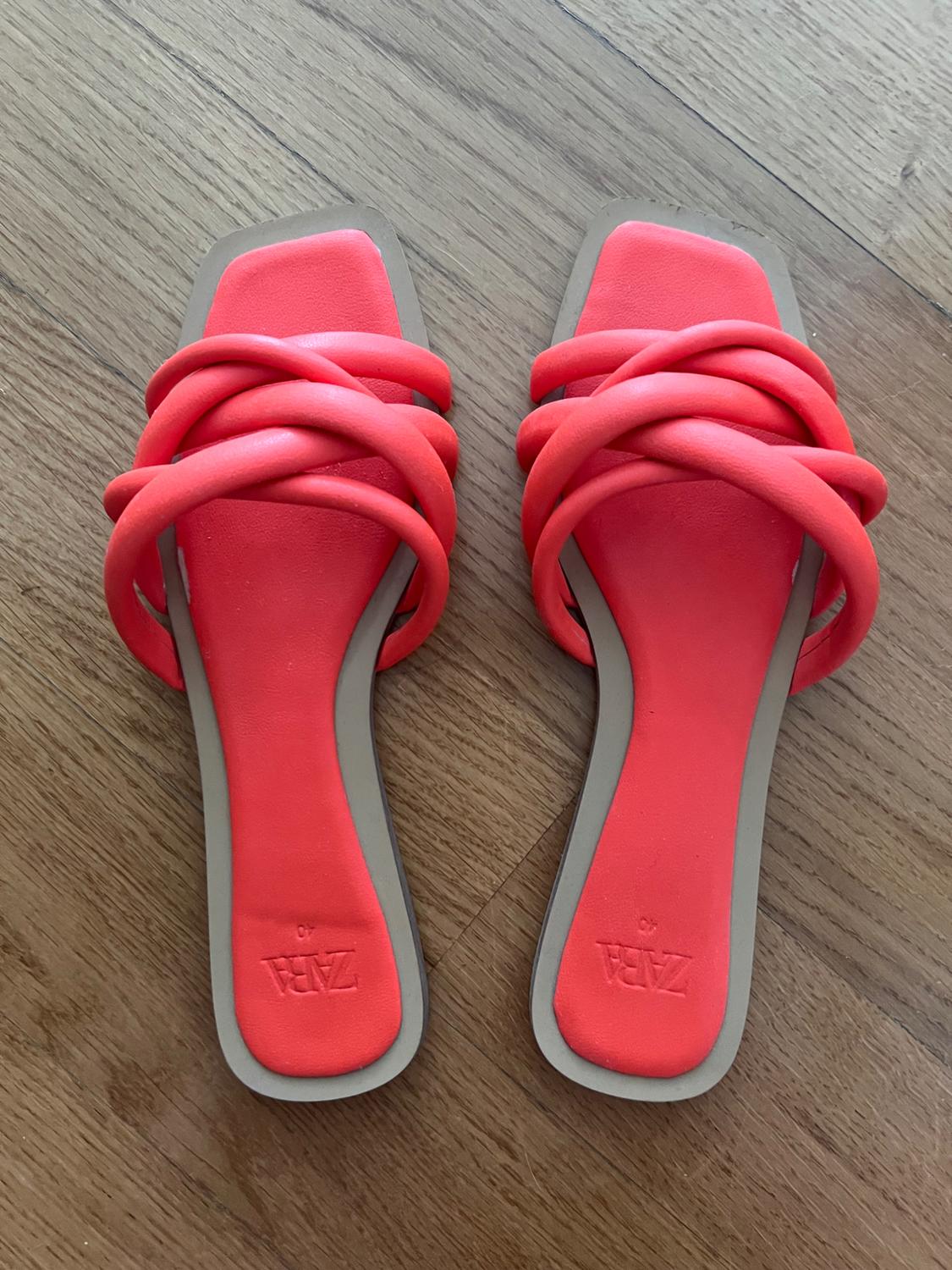 Coral-coloured flat sandals with tubular crossover straps on a wooden floor. Visible text: ZARA 40.