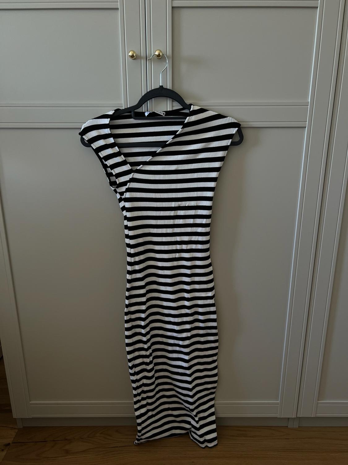 Black and white horizontal striped bodycon dress with an asymmetric neckline, hanging in a light grey wardrobe with gold handles.