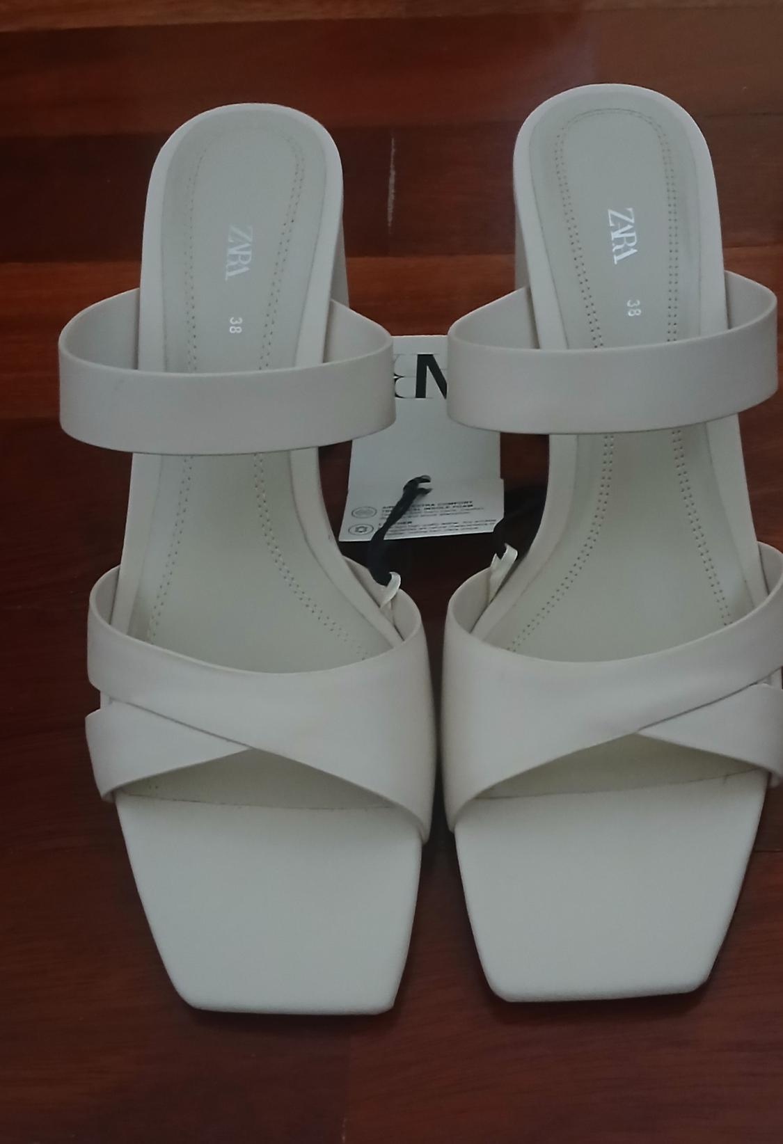 White block heel sandals with cross-over straps and visible label. "ZARA" brand and size "38" printed on the insole.