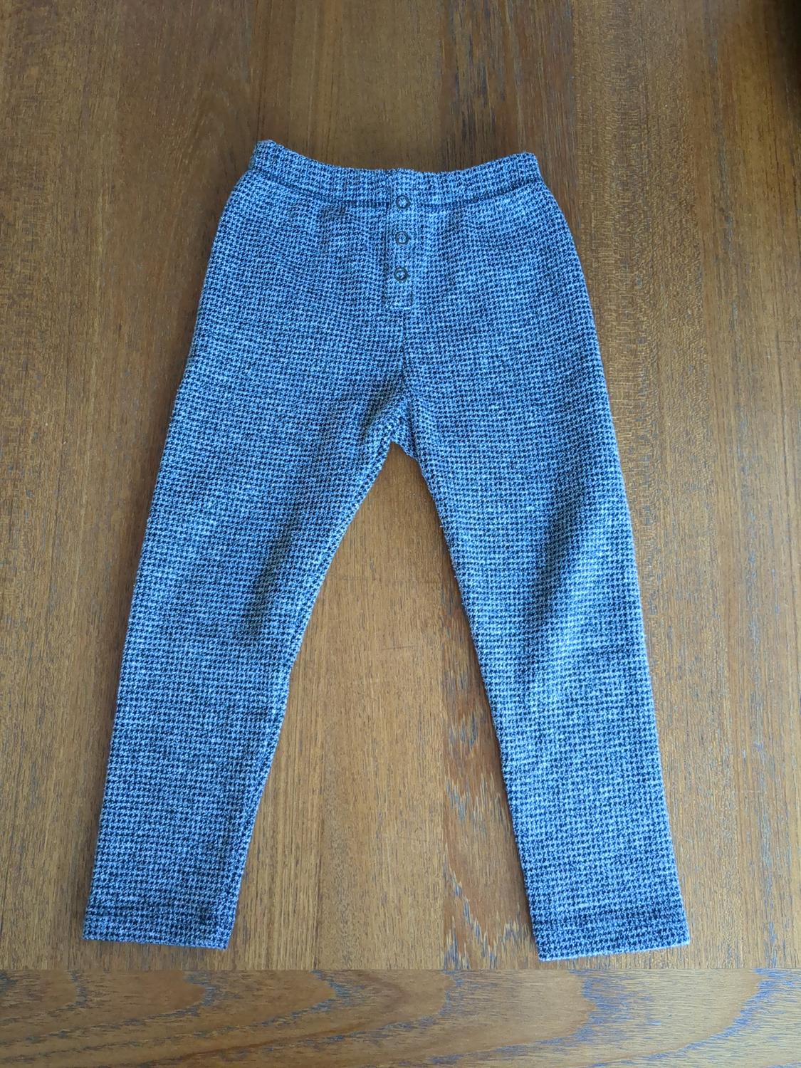 Gray fabric pants with a small plaid pattern and buttons on the front, on a wooden surface.