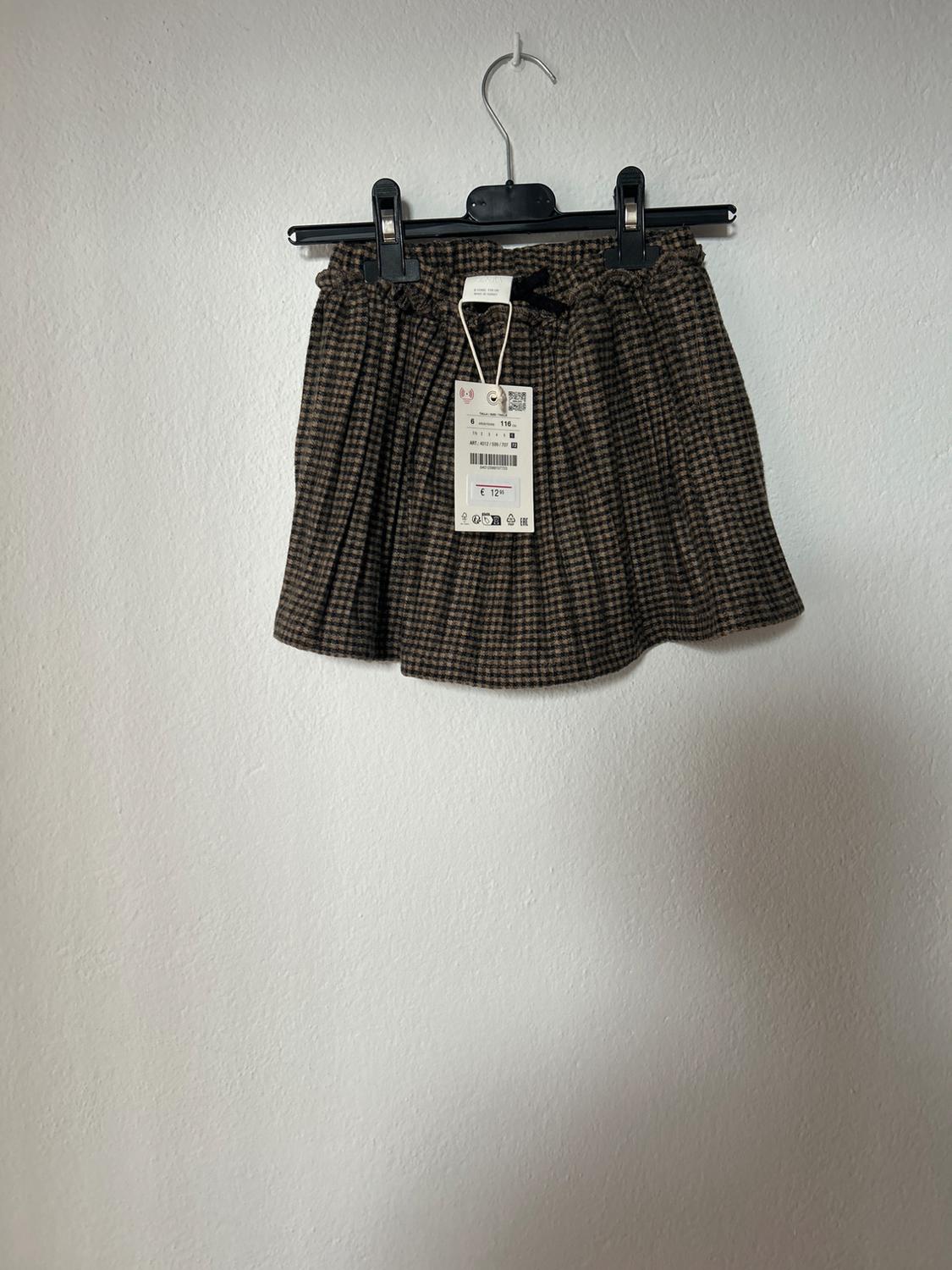 Brown checked mini skirt hanging on a black hanger against a white wall. Visible tag with a price of £12.
