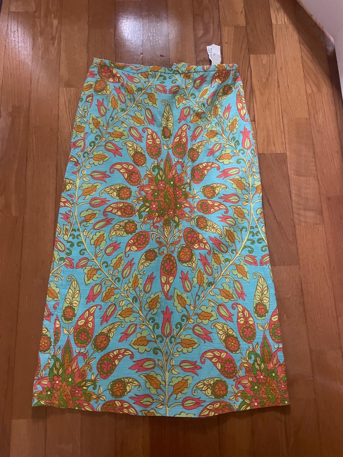 Long skirt with floral print in shades of blue, red and yellow on a wooden floor. Label visible at the top.