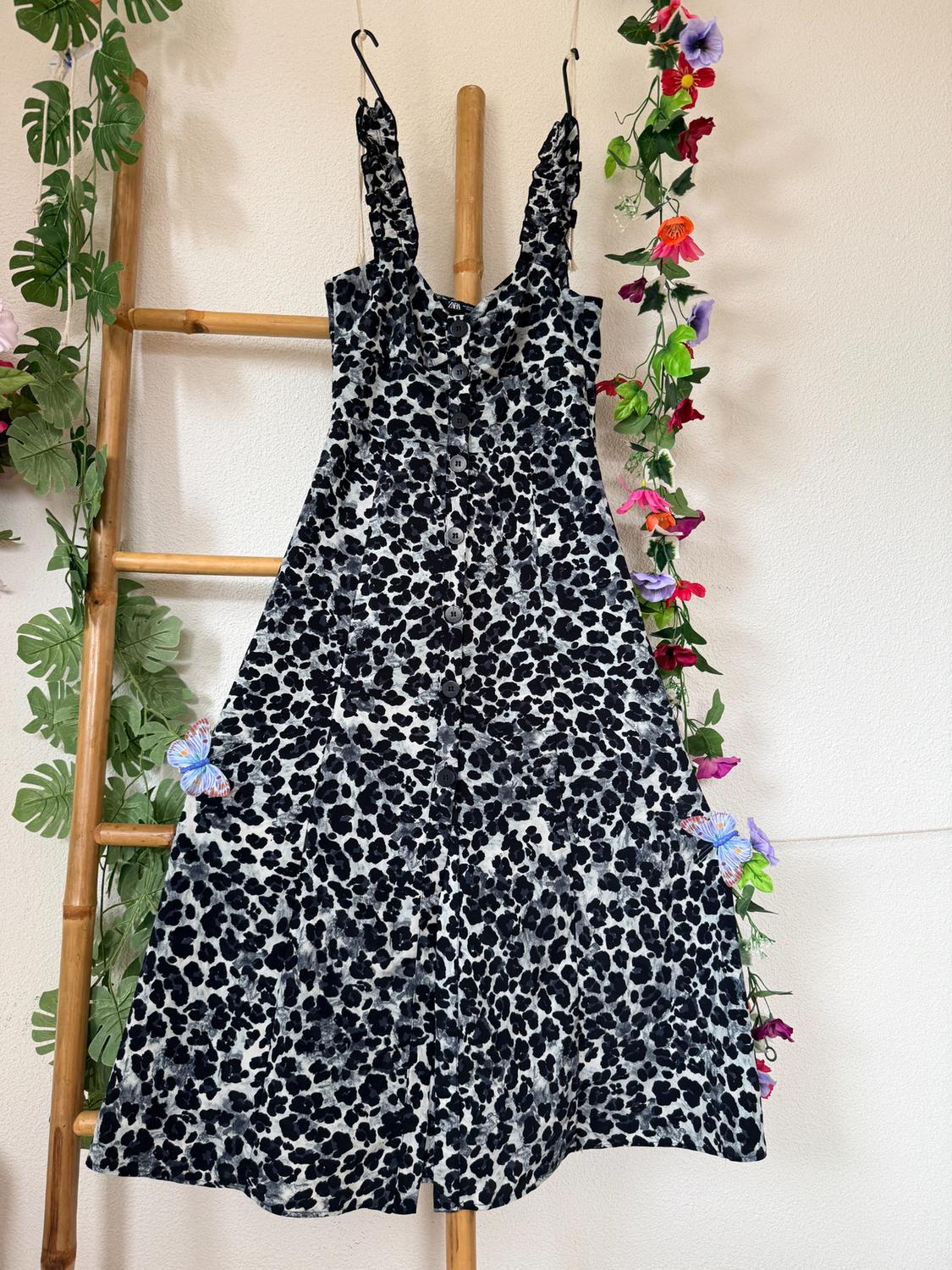 Black and white spot print camisole dress hanging on a bamboo ladder, decorated with leaves and flowers.
