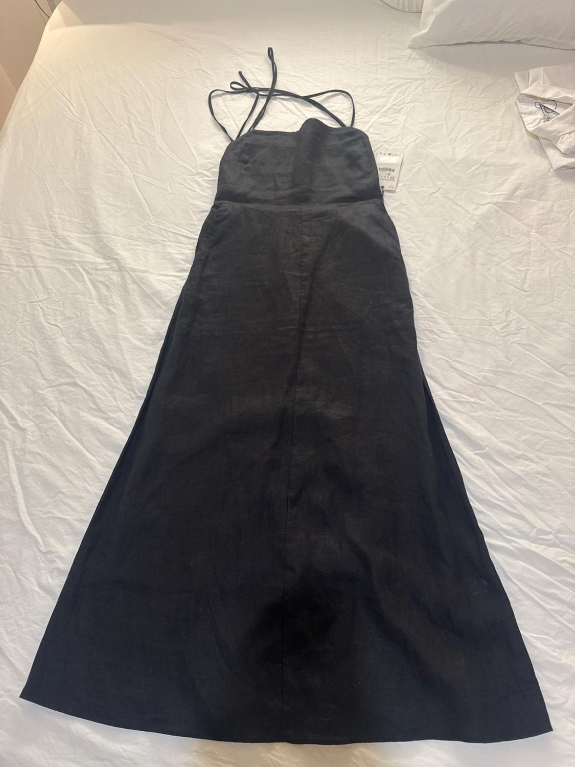Black dress with thin crossed straps, spread out on a white bed. Label visible on the right side of the dress.