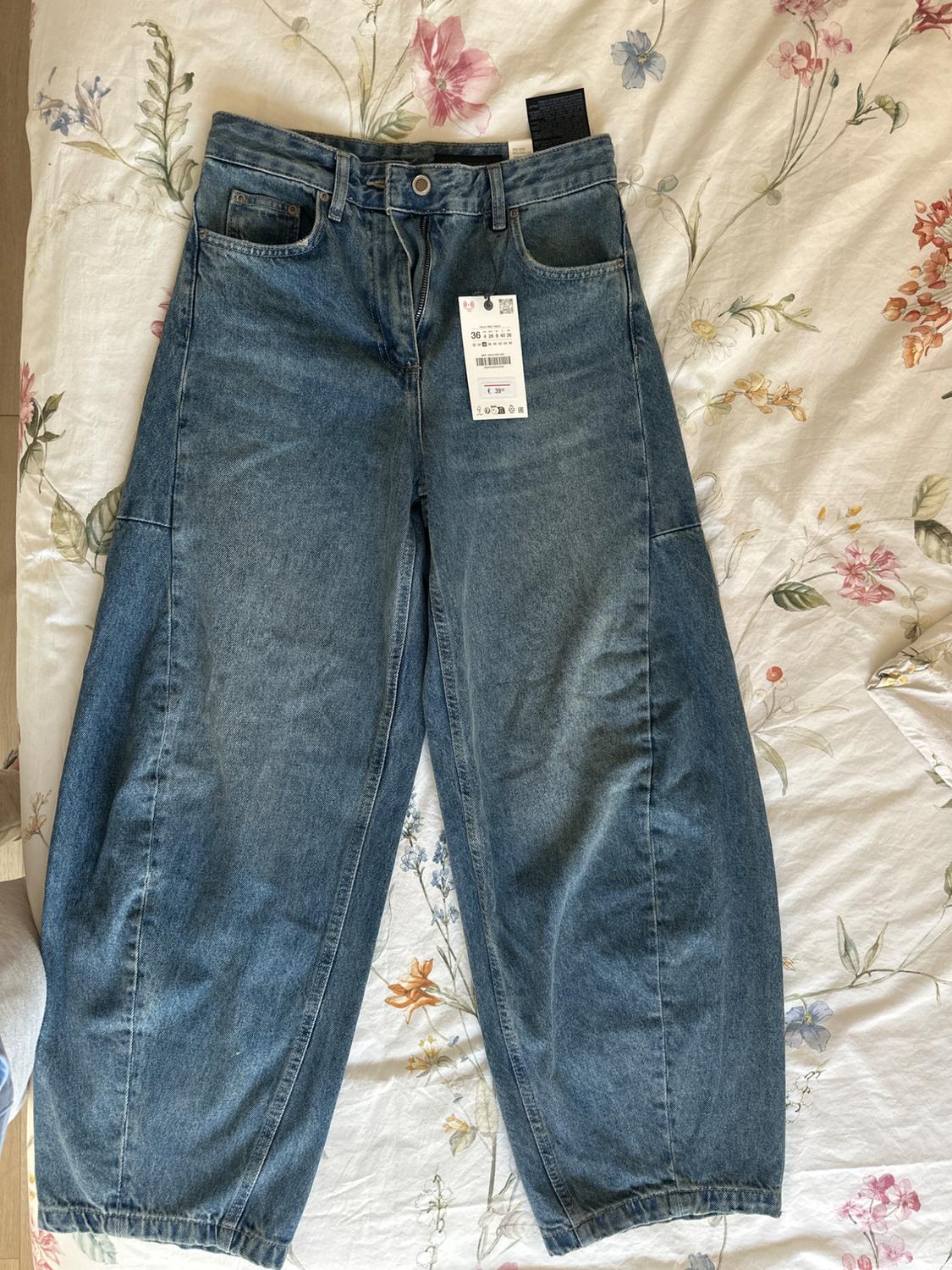 Wide-leg blue jeans with price tag on a white floral-print bedspread.