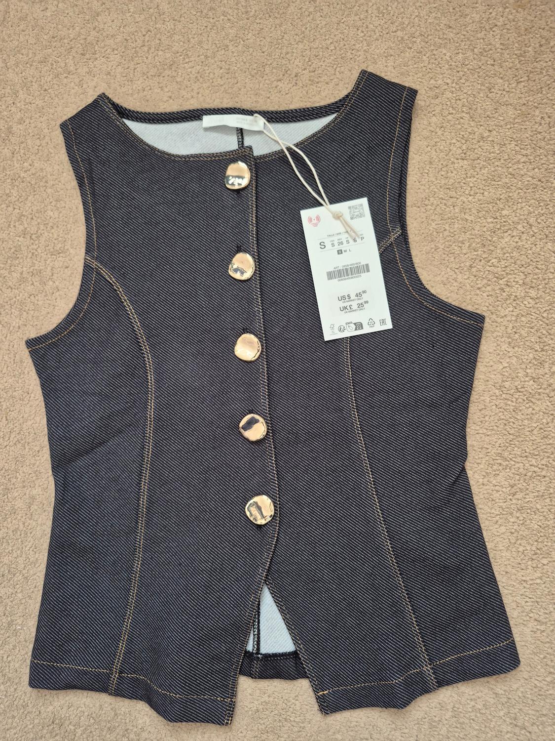 Dark blue denim waistcoat with gold buttons and US$45 price tag, on a beige background.
